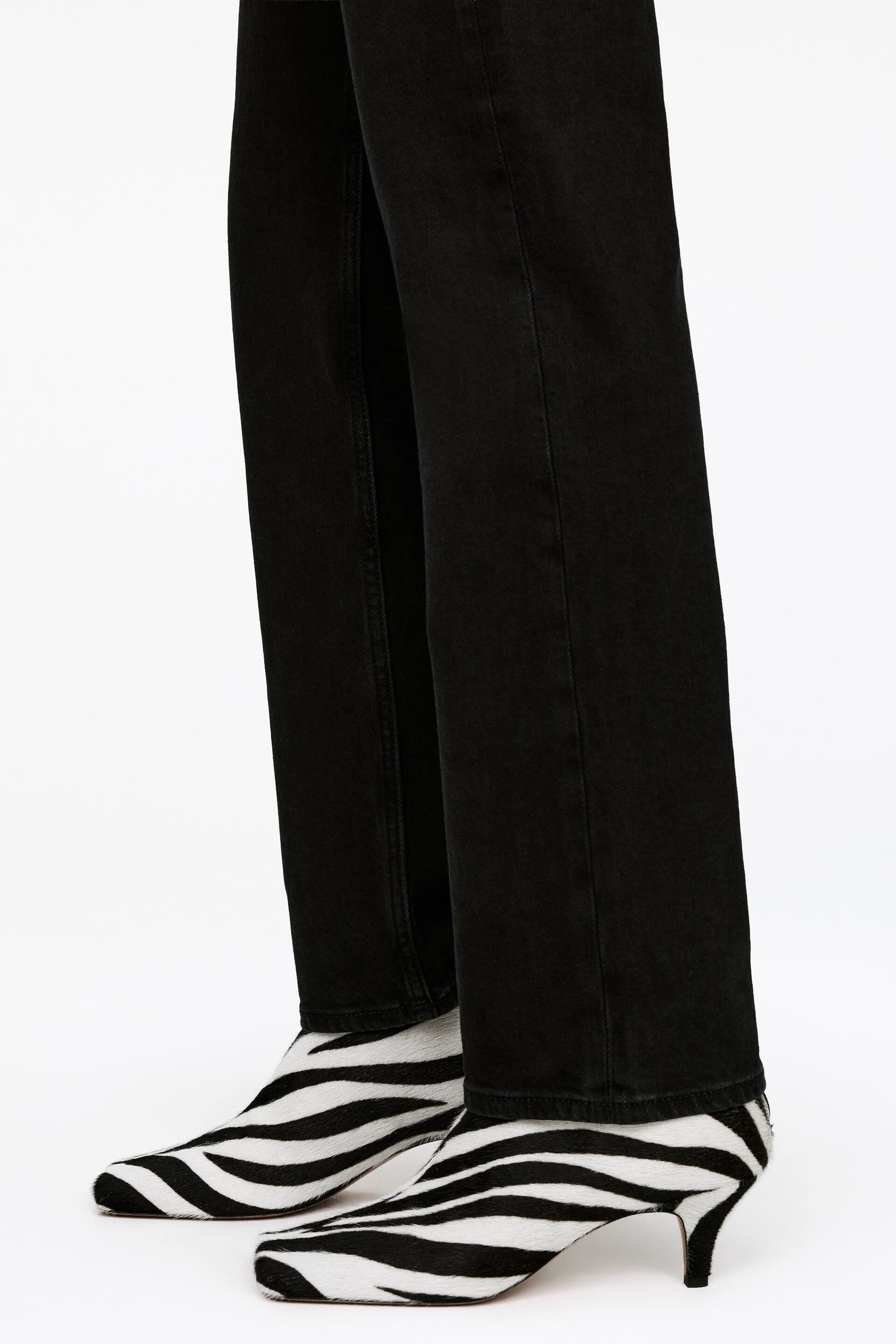 View larger image: Zebra print ankle boots are paired with black straight-leg trousers, visible from a front-side angle. The boots feature a pointed square toe, a kitten heel, and a black and white striped pattern.