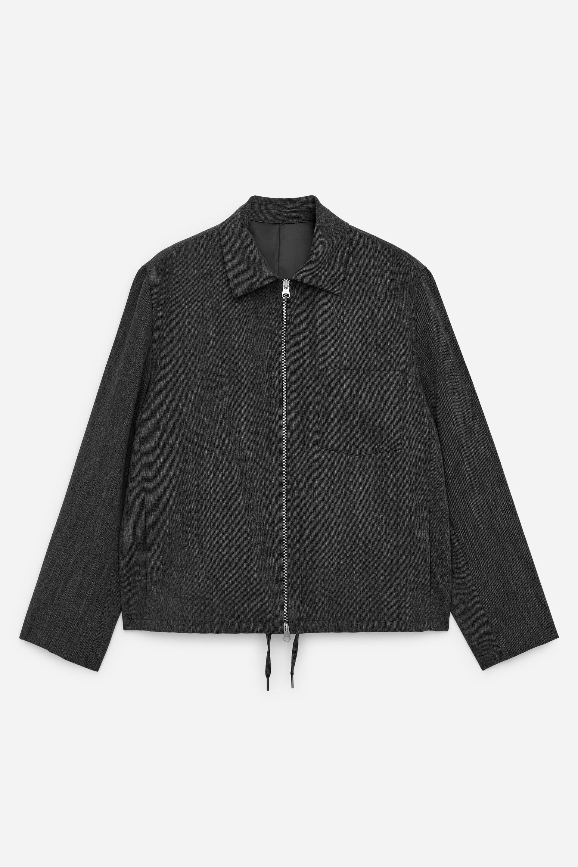 Zobacz większy obraz: Ciemnoszara, dopasowana wełniana marynarka jest prezentowana, przodem do widza, z klasycznym kołnierzem i dwukierunkowym zamkiem błyskawicznym w srebrnym odcieniu, umieszczonym na środku. Kieszeń naszywana na lewej piersi ma materiał w kontrastowym kierunku, a sznurki ściągające zwisają z dolnego brzegu.