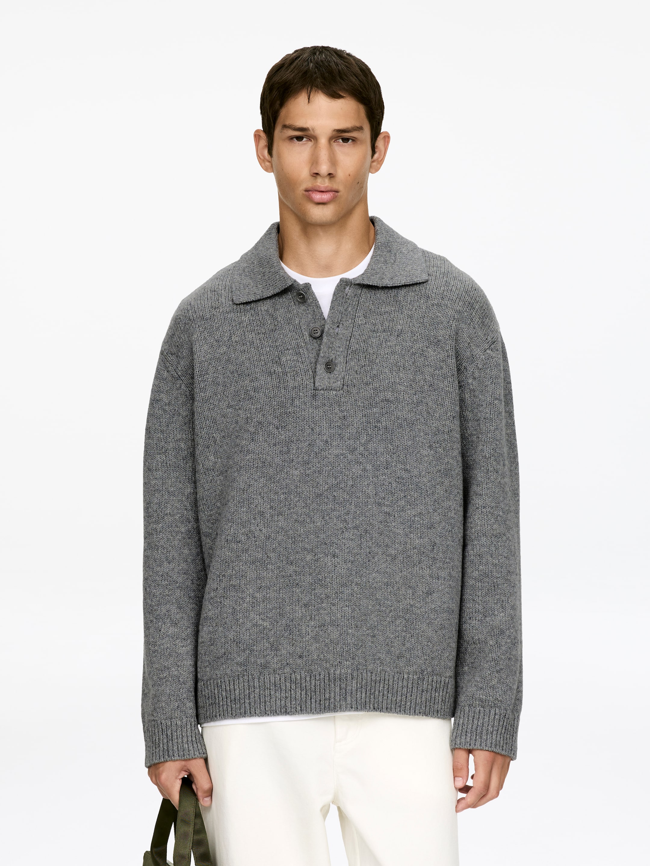 Agrandir l'image: Un polo en tricot gris est présenté de face, doté d'un col polo et d'une patte de boutonnage à trois boutons gris foncé. Ce haut en tricot est porté par-dessus un t-shirt blanc, affichant un ourlet et des poignets en côtes.
