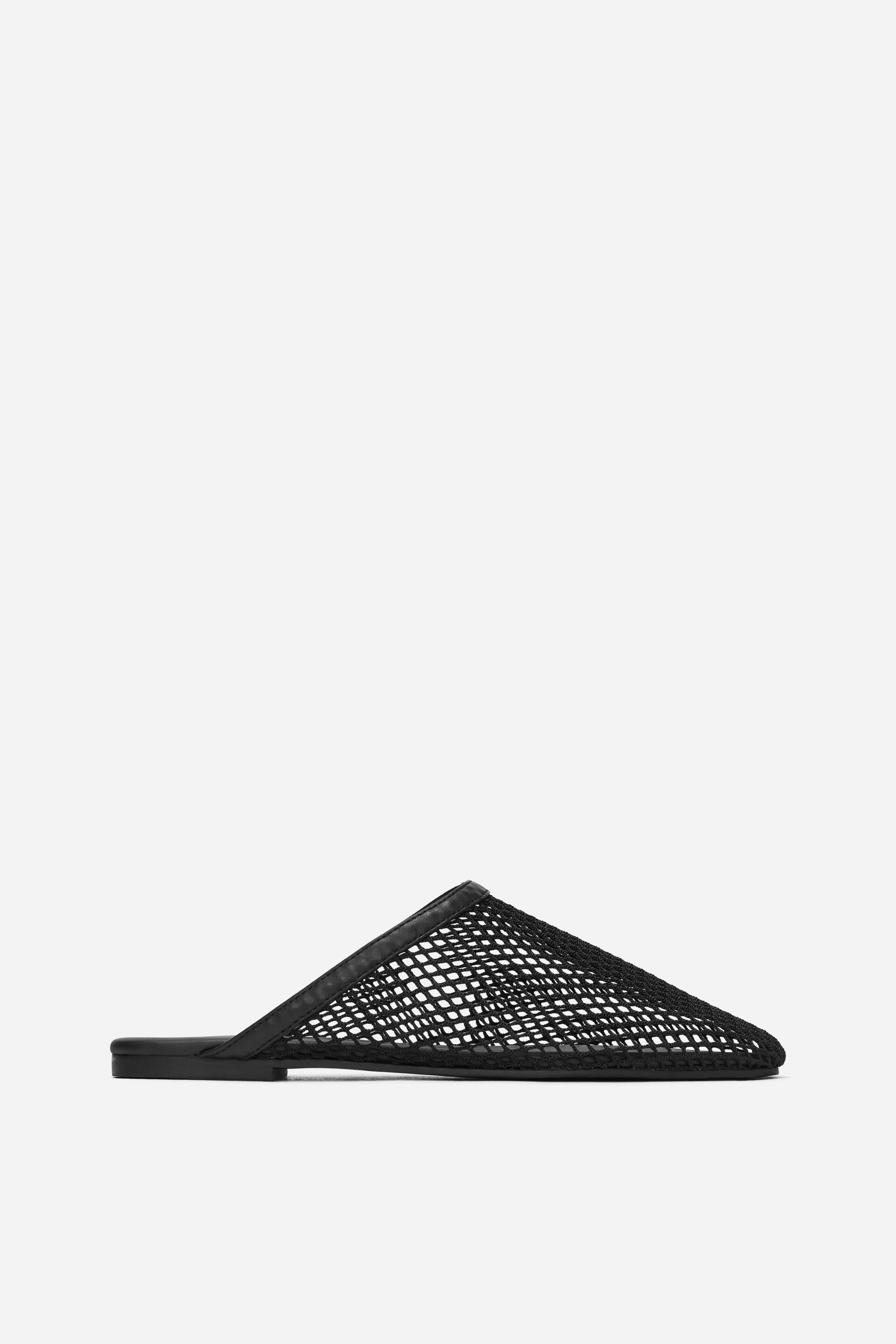 Vis større bilde: En svart netting-mulesko vender mot venstre, med en flat såle og en spiss tå. Overdelen har et strukturert, åpent nettingdesign, avsluttet med en glatt kant rundt åpningen ved foten.