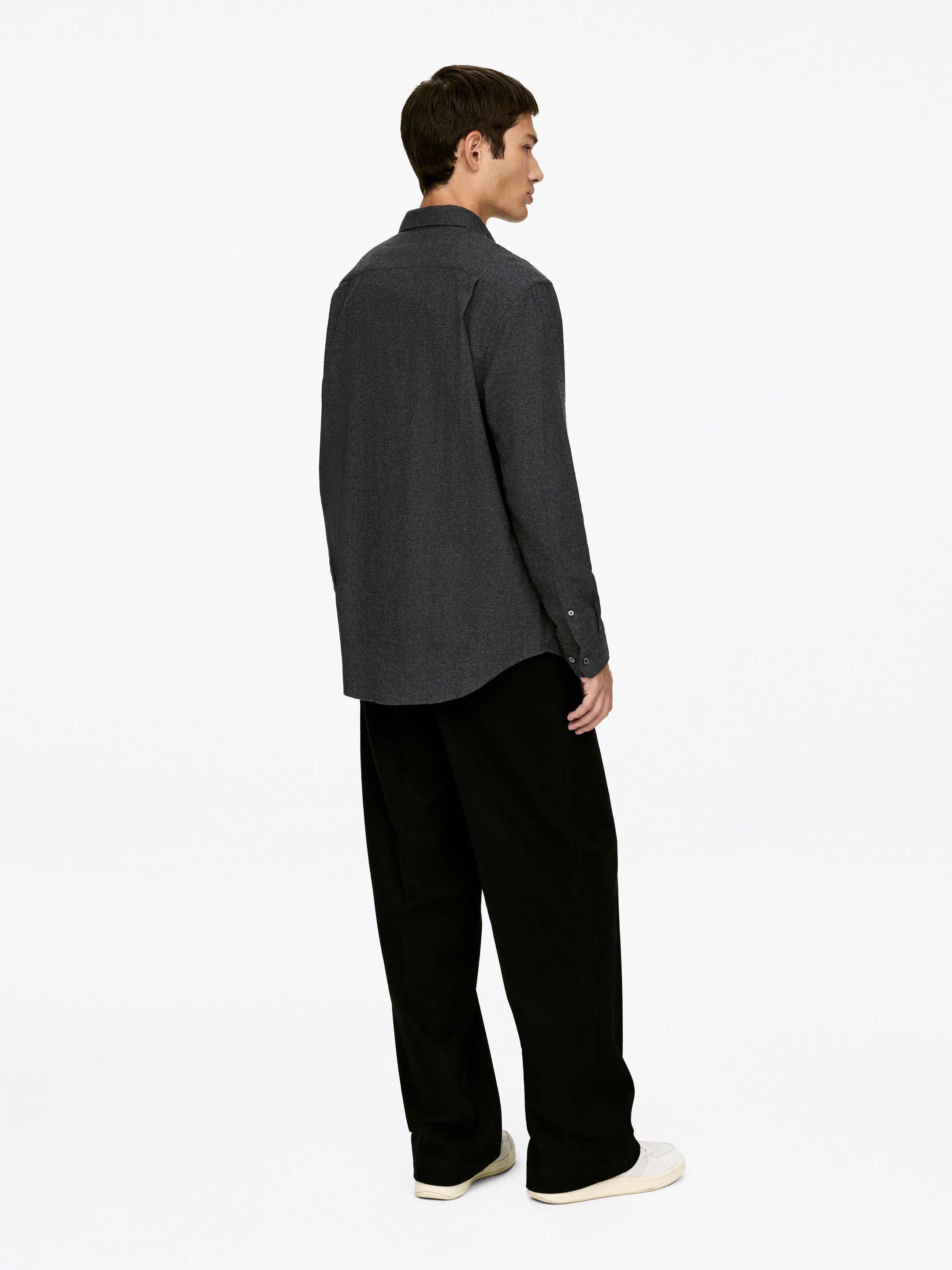Agrandir l'image: Une chemise en flanelle de coton gris foncé avec une coupe décontractée est portée par le mannequin. La chemise à manches longues est déboutonnée.