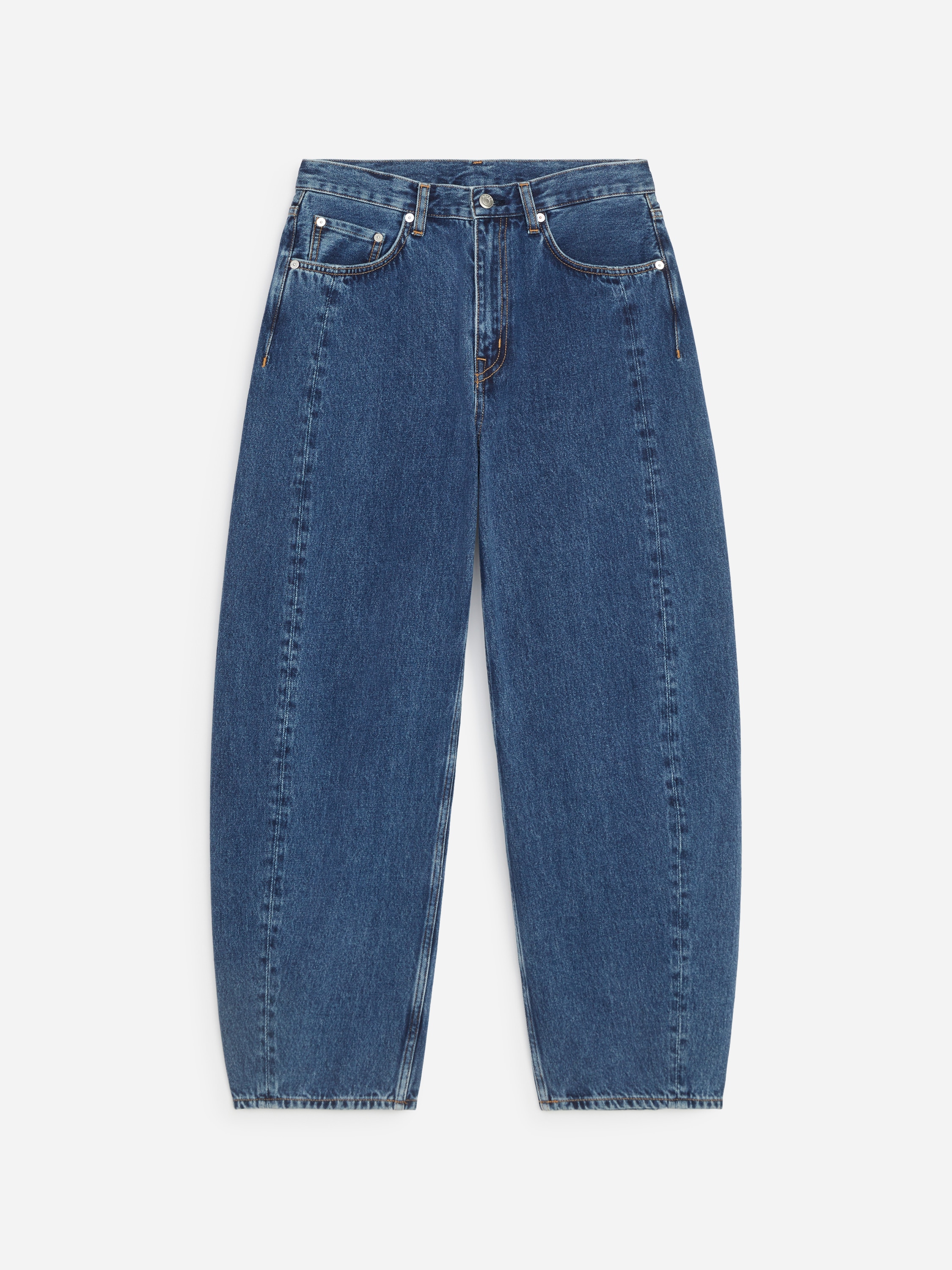 Model ma na sobie niebieskie dÅ¼insy z denimu o swobodnym kroju i profilowanych, lekko wygiÄtych nogawkach. DÅ¼insy zestawiono z granatowym swetrem z okrÄgÅym dekoltem, noszonym na biaÅej koszuli z koÅnierzykiem, oraz ciemnobrÄzowymi loafersami.