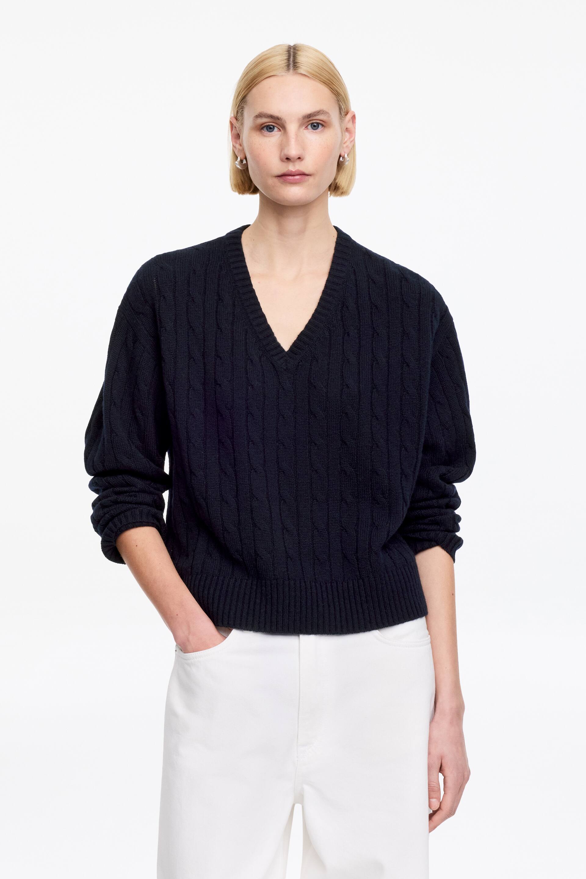 Ver imagen más grande: Un jersey de punto trenzado de cuello en V azul oscuro se presenta de frente, mostrando un ajuste relajado con un dobladillo acanalado y puños acanalados.