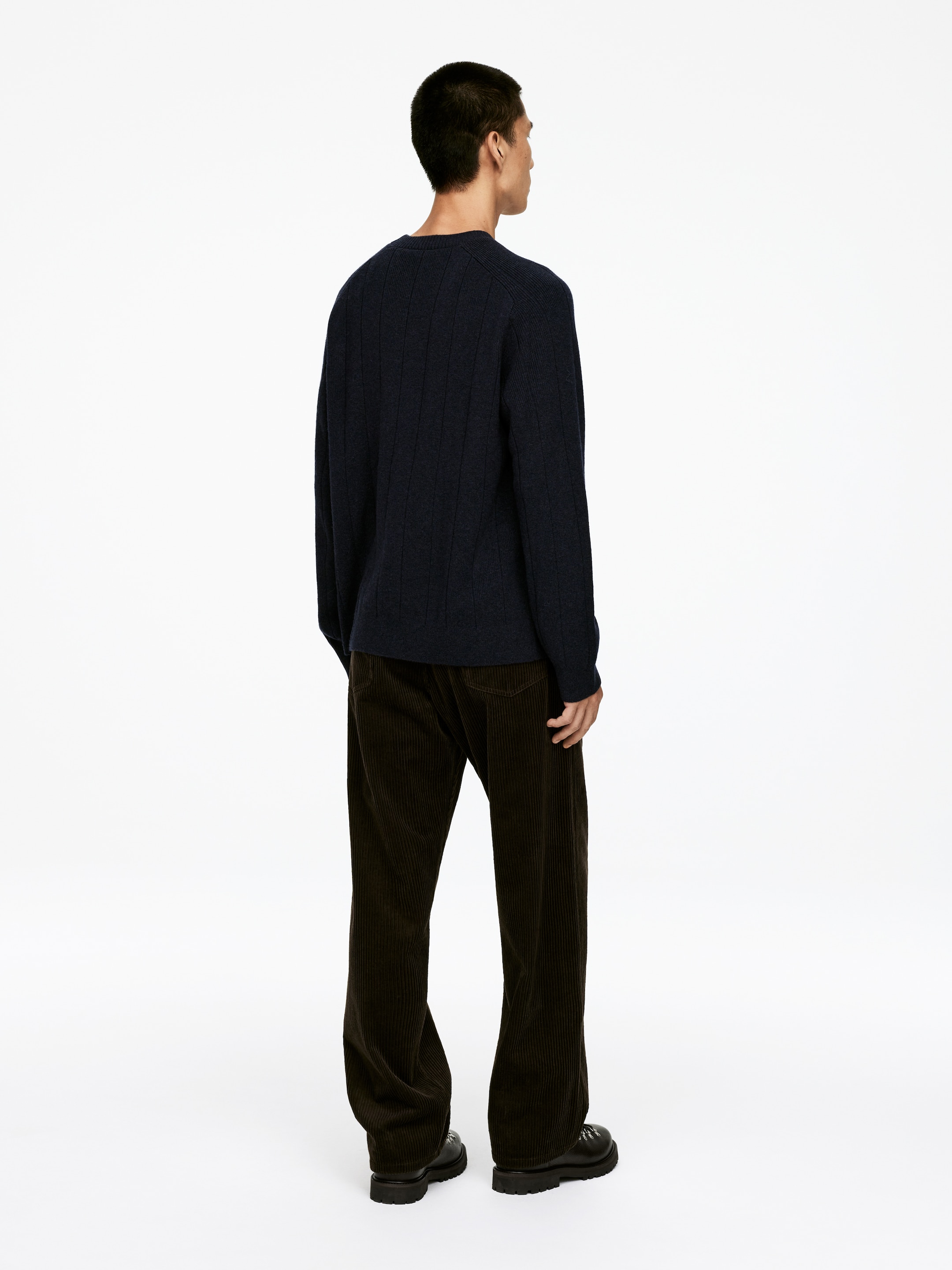 View larger image: A dark blue sweater, featuring a distinct vertical ribbed knit pattern on the back, is being worn with dark brown wide-leg corduroy pants, which display prominent vertical wales. The garments are being presented from a rear view, highlighting their fit and design.