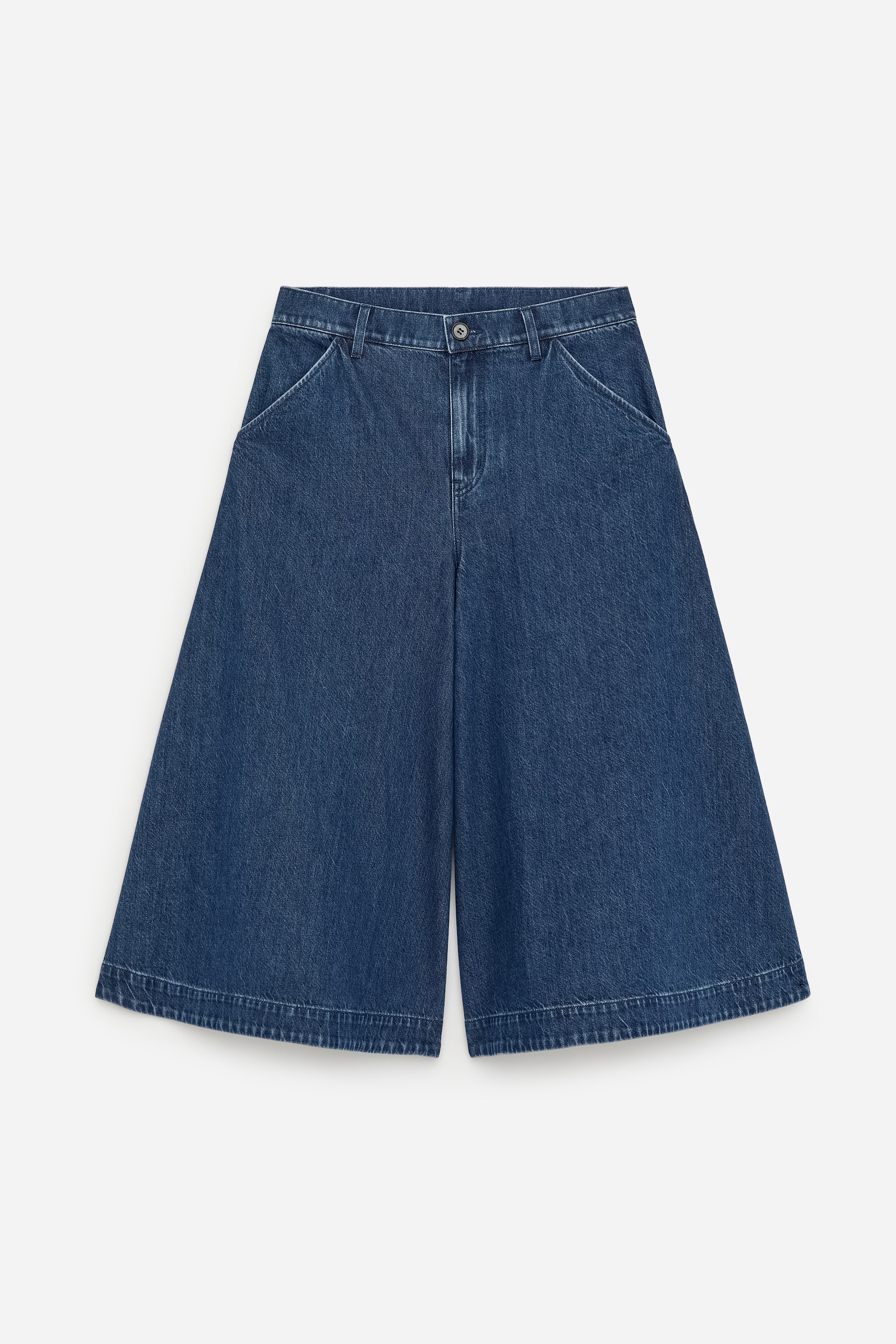 Agrandir l'image: Devant, des culottes en denim bleu présentent une taille haute avec une fermeture à bouton unique et deux poches avant en biais, offrant une silhouette à jambes larges et raccourcies, et se terminant par des ourlets cousus visibles.