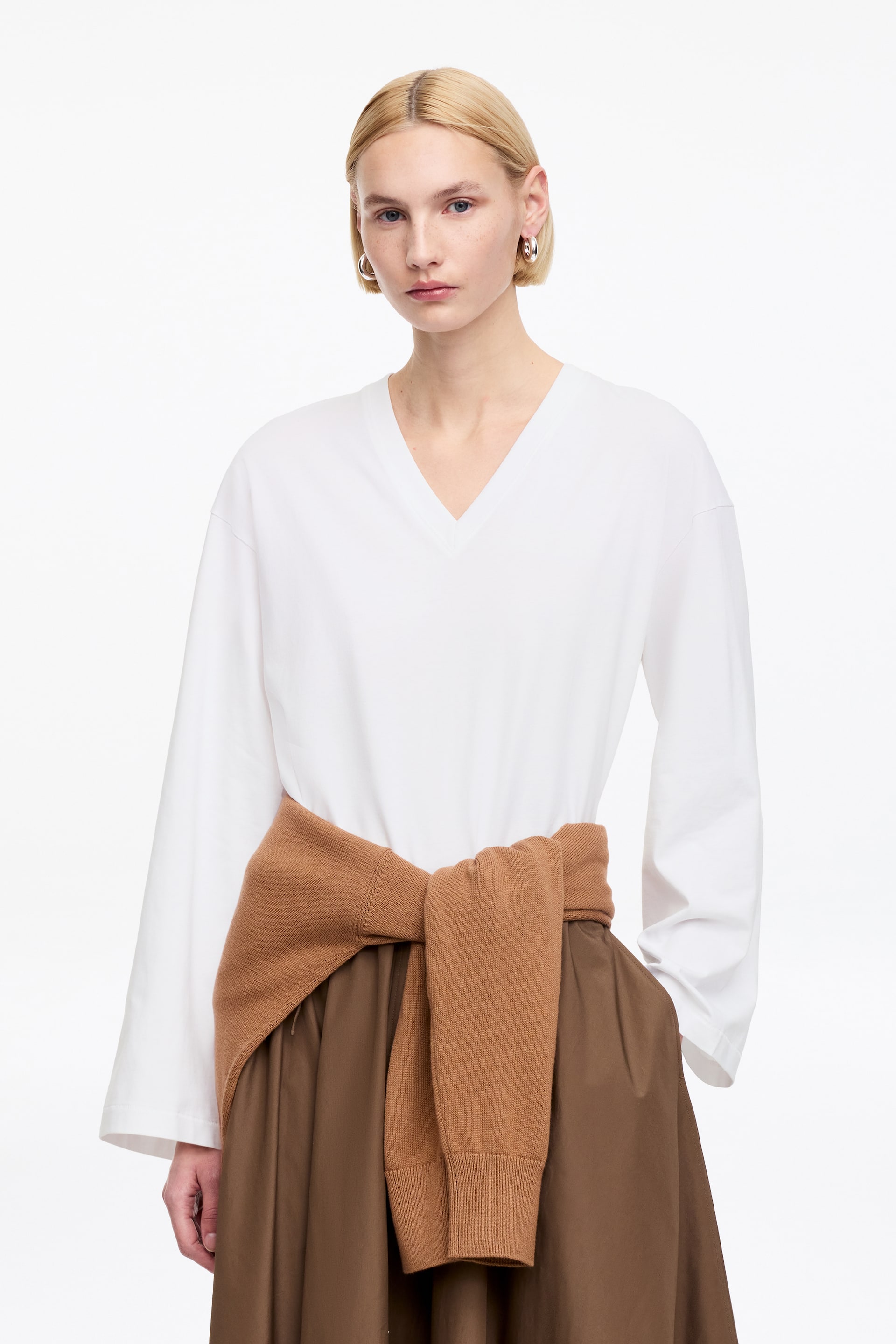 Ver imagen más grande: Un top blanco de manga larga está de frente, con un escote en V y un corte holgado con mangas anchas y sueltas.