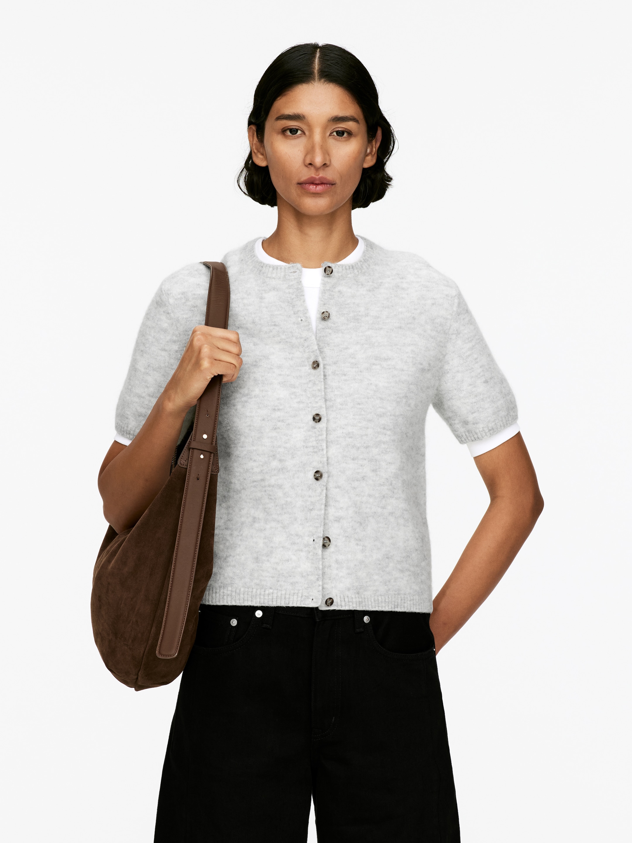 Visualizza immagine più grande: Un cardigan a maniche corte grigio chiaro viene presentato, caratterizzato da una texture a maglia pelosa e da uno scollo rotondo. È progettato con una chiusura frontale a bottoni, che presenta diversi bottoni scuri e circolari, ed è arricchito da maniche corte leggermente a sbuffo con polsini a coste e un orlo a coste, sovrapposto a una t-shirt bianca.