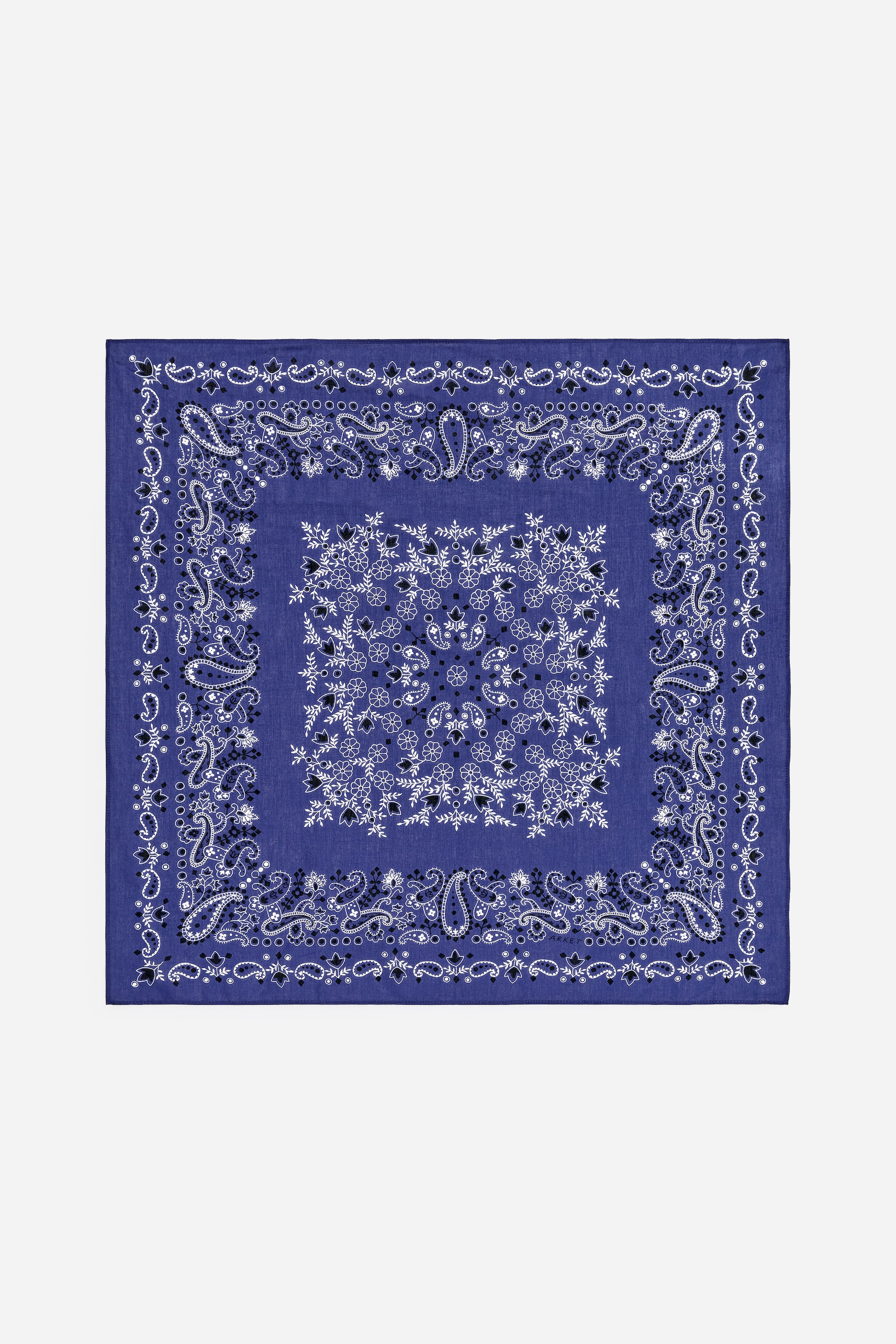 Agrandir l'image: Un bandana bleu est posé à plat, mettant en valeur un motif paisley blanc et noir. Le motif présente un carré central de motifs floraux et de feuilles blancs, entouré d'une bordure de gouttes paisley blanches et noires et de points. Une bordure extérieure composée de petits éléments floraux et paisley répétés encadre le dessin.