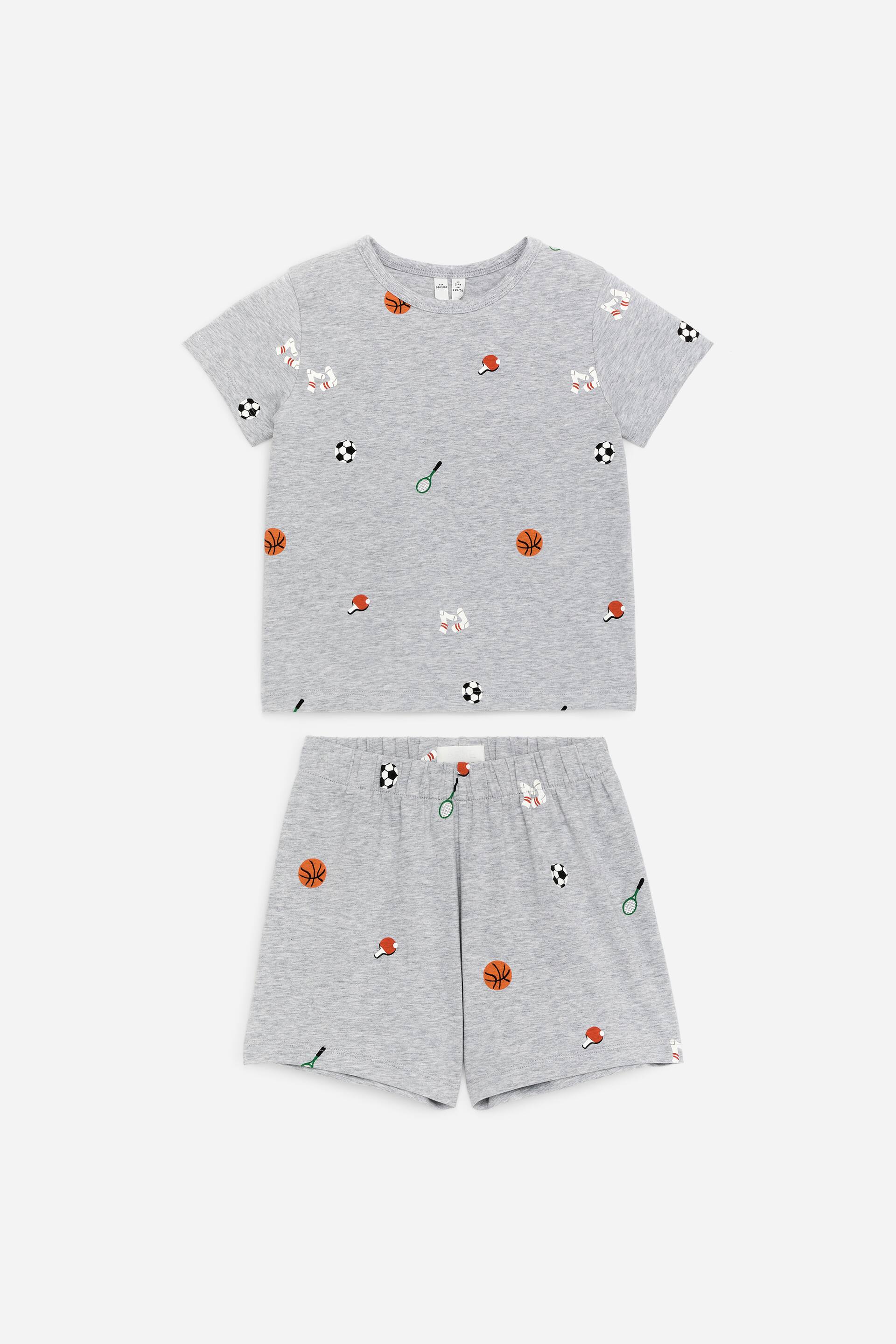 View larger image: A grey pyjama set, displayed FRONT, features a regular-fit T-shirt and shorts, both crafted from cotton jersey with a subtle ribbed texture. The set showcases an all-over pattern of various sports equipment, including basketballs, footballs, tennis rackets, table tennis paddles, and baseball gloves. The T-shirt boasts a round neck, while the shorts are designed with an elasticated waist.