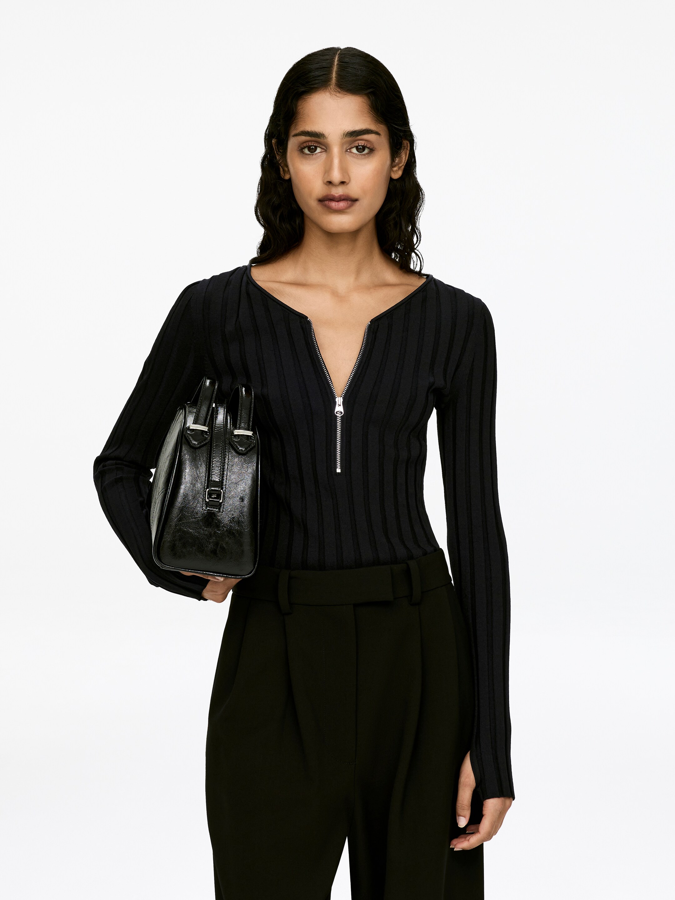 View larger image: A black rib-knit, slim-fit, long-sleeved jumper featuring a half zip at the centre front is being worn by the model. The model is also wearing black trousers, completing the outfit.