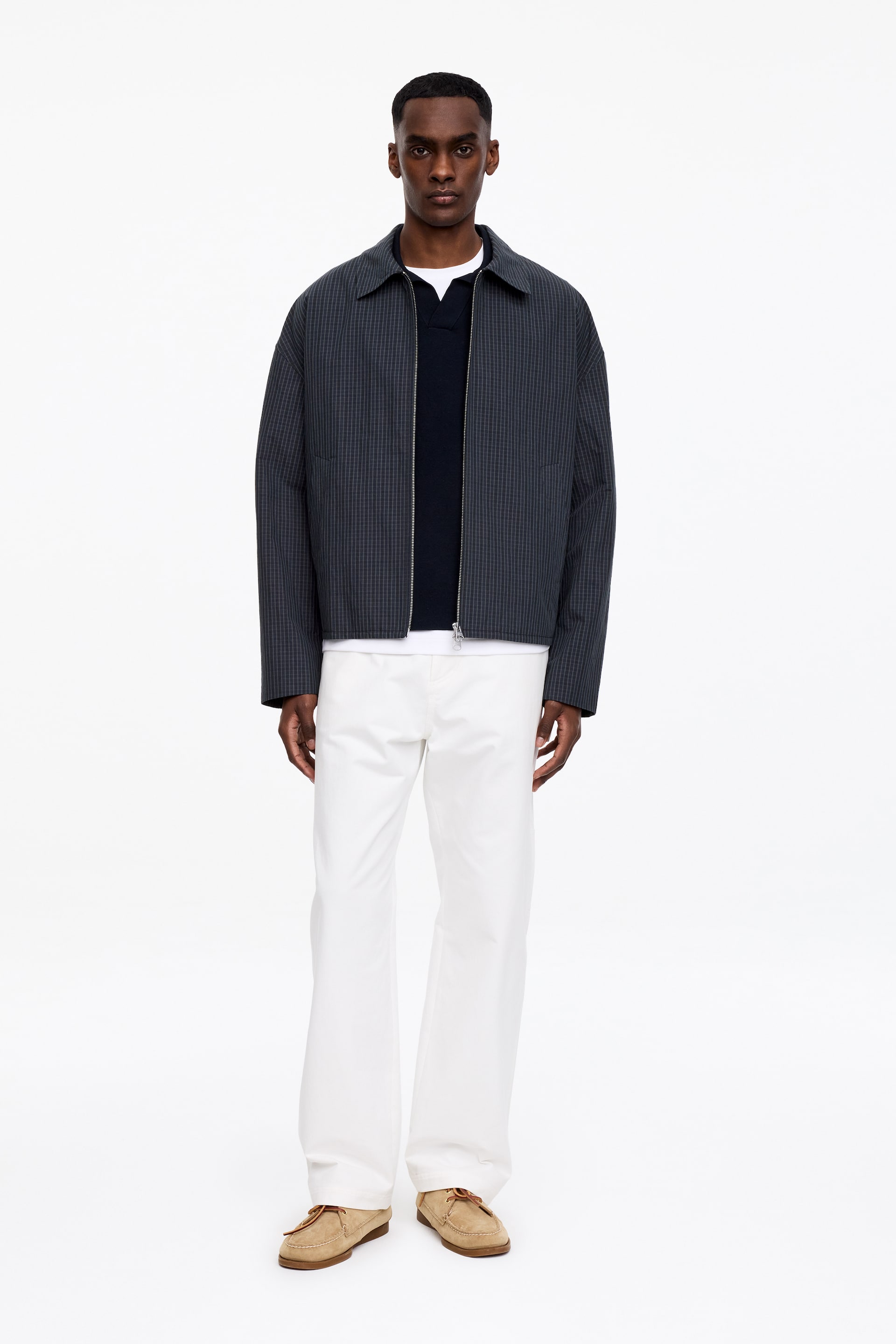 Zobraziť väčší obrázok: Tmavosivá bunda s jemným mikro-kockovaným vzorom je prezentovaná z prednej strany, s rozloženým golierom a strieborným zipsom po celej dĺžke, nosená otvorená cez biele tričko s okrúhlym výstrihom a tmavomodrý sveter s výstrihom do V.