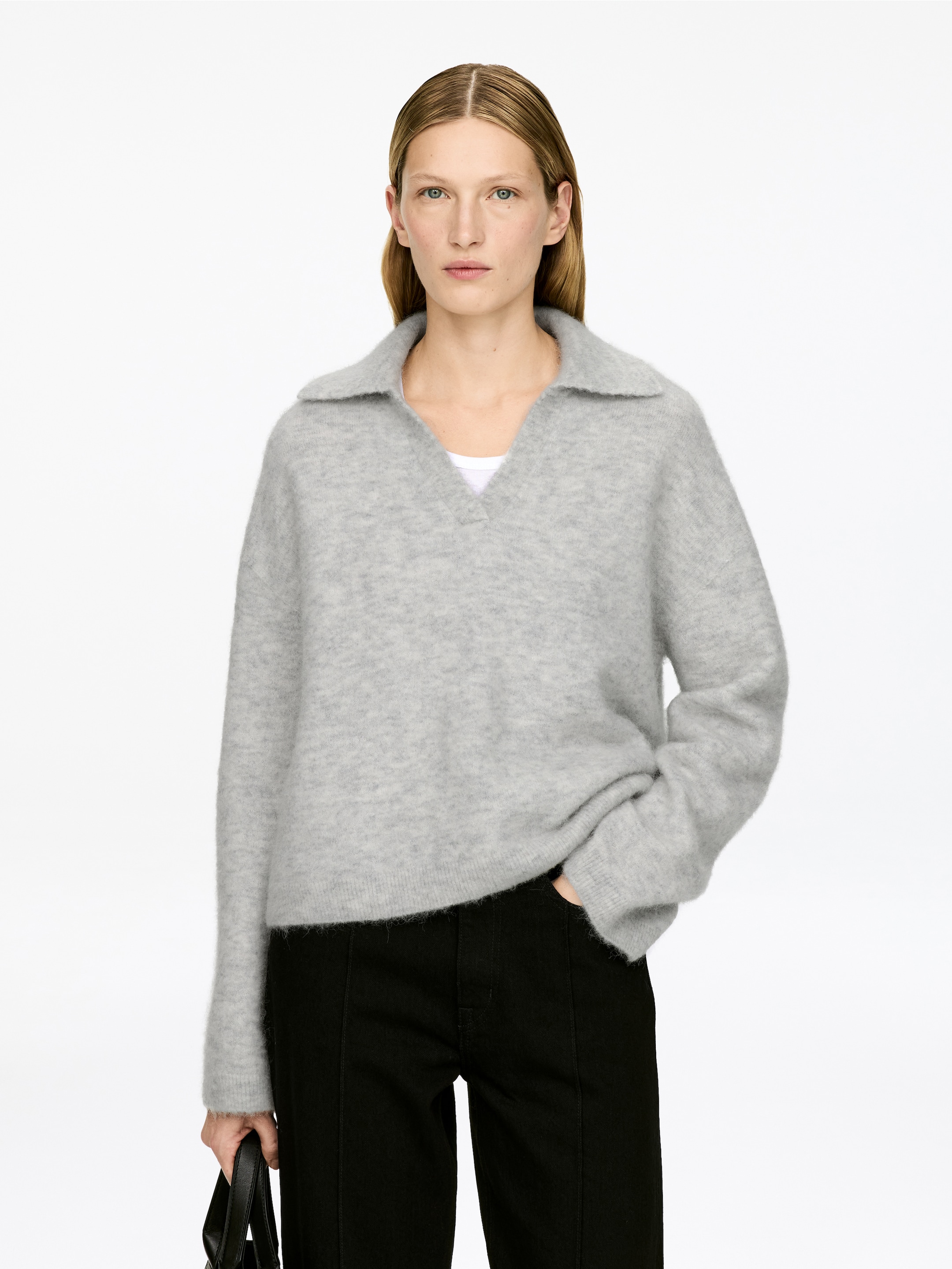 Agrandir l'image: Un pull en laine gris flou est orienté vers l'avant, avec un col pointu ouvert et une ouverture en V. Il présente une coupe décontractée avec des manches longues et un ourlet droit, et un t-shirt blanc est visible en dessous.