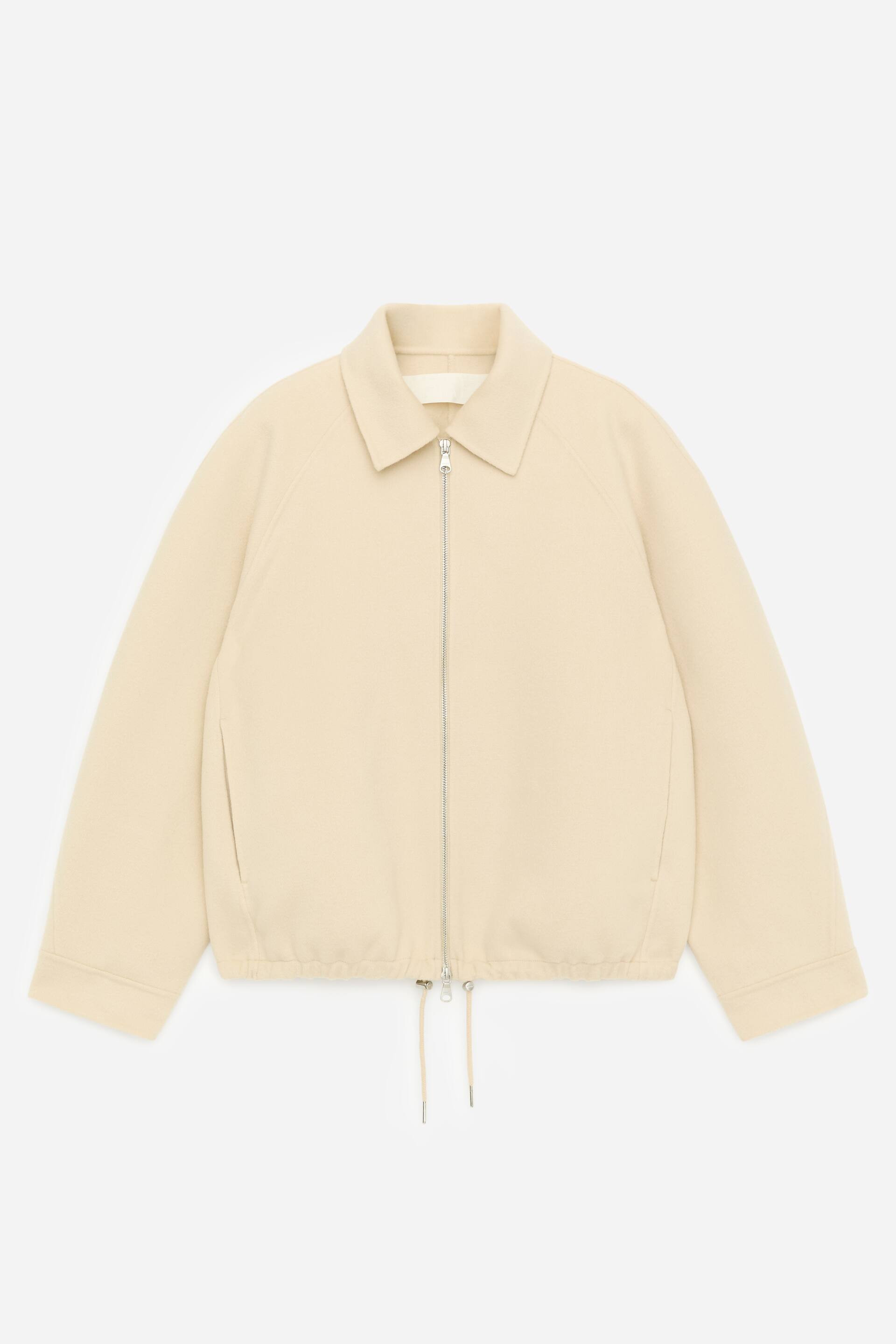 Größeres Bild anzeigen: Eine hellbeige Jacke wird in der Vorderansicht präsentiert, mit einem spitzen Kragen, einem silberfarbenen Reißverschluss in voller Länge, Raglanärmeln, zwei dezenten Seitentaschen und einem Kordelzugsaum mit silberfarbenen Endkappen.
