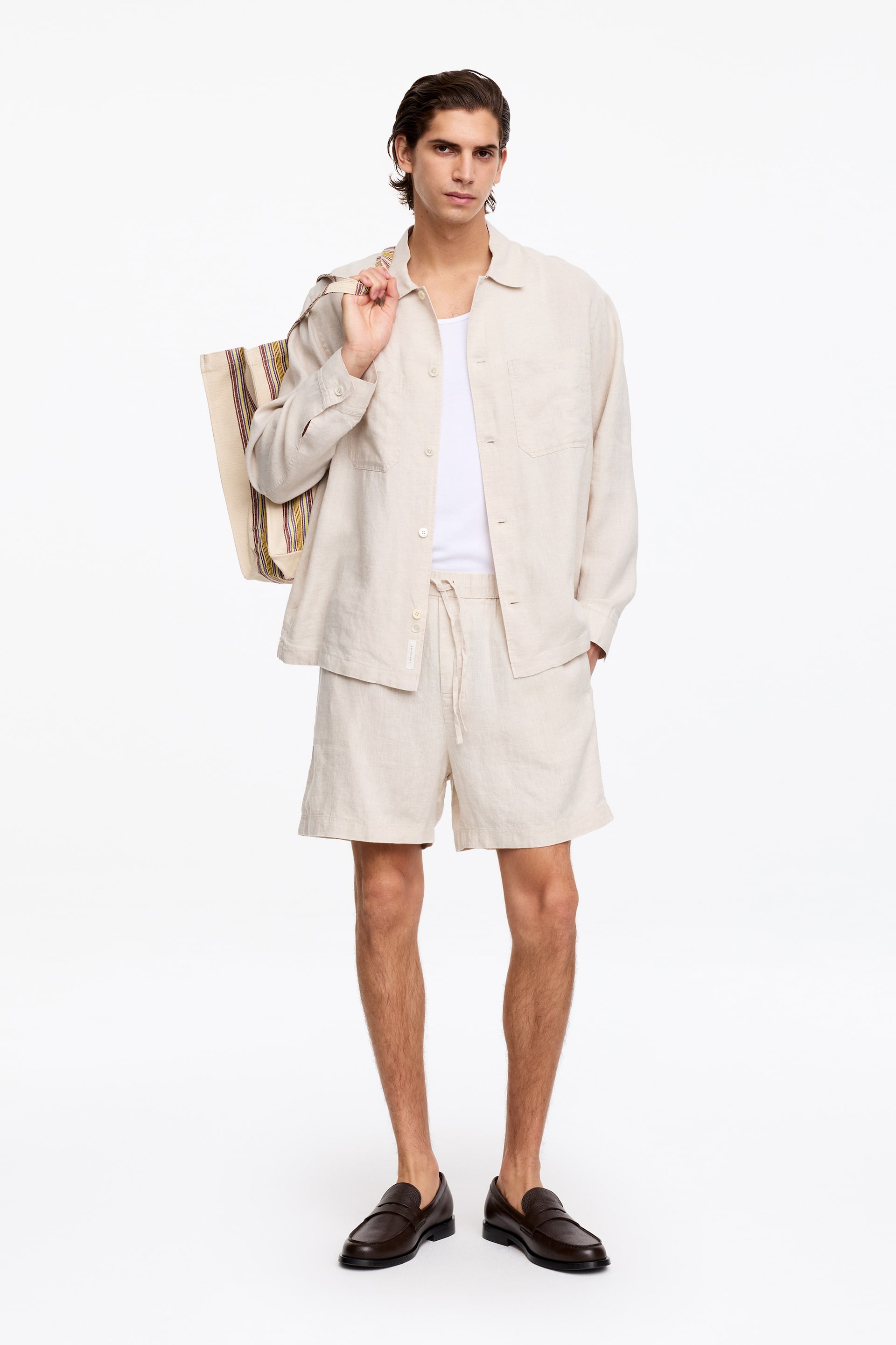 Grotere afbeelding bekijken: De model draagt licht beige regular fit linnen shorts, met een pull-on stijl met een elastische tailleband met trekkoord en zijnaadzakken. Het model staat met één hand in een zak.