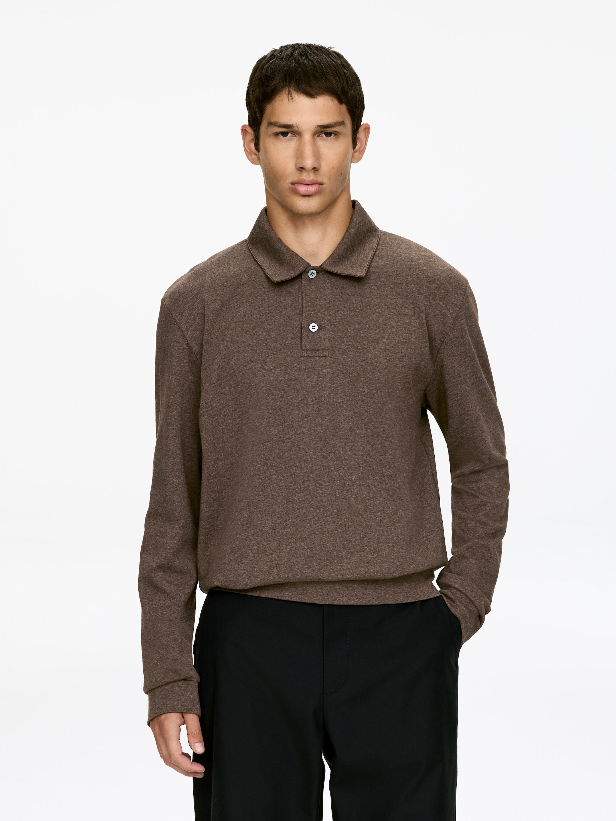 Grotere afbeelding bekijken: Een langharige poloshirt met lange mouwen in een gevlekte bruine kleur wordt recht naar voren gepresenteerd. Het heeft een spread kraag en een placket met twee lichtgekleurde knopen. De lange mouwen eindigen in eenvoudige manchetten, en de zoom rust over zwarte broeken met een licht geplooid effect.
