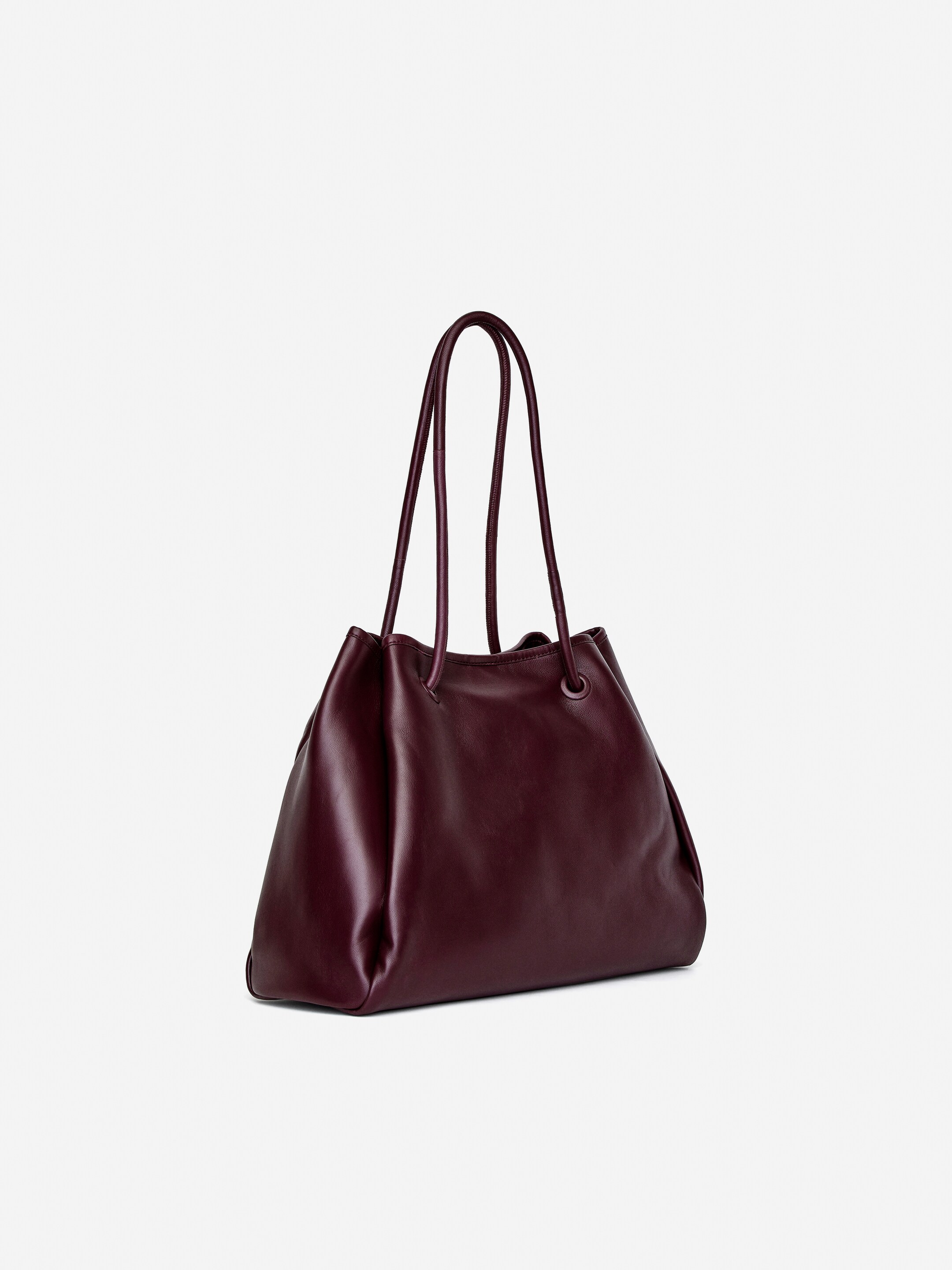 Agrandir l'image: Un sac fourre-tout en cuir bordeaux foncé est présenté sous un angle latéral gauche, mettant en valeur sa forme souple et non structurée avec de doux plis. Il est doté de deux poignées supérieures fines qui se tiennent droites.