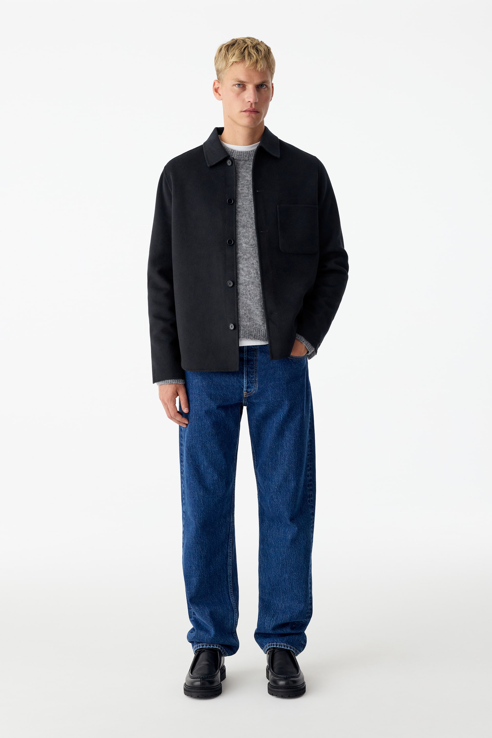Ver imagem maior: Uma sobrecamisa preta em mistura de lã, com gola clássica e um único bolso de chapa no peito, é usada aberta pela modelo. A sobrecamisa está coordenada sobre uma camisola de malha cinzenta e jeans azuis para evidenciar o seu corte descontraído e regular.