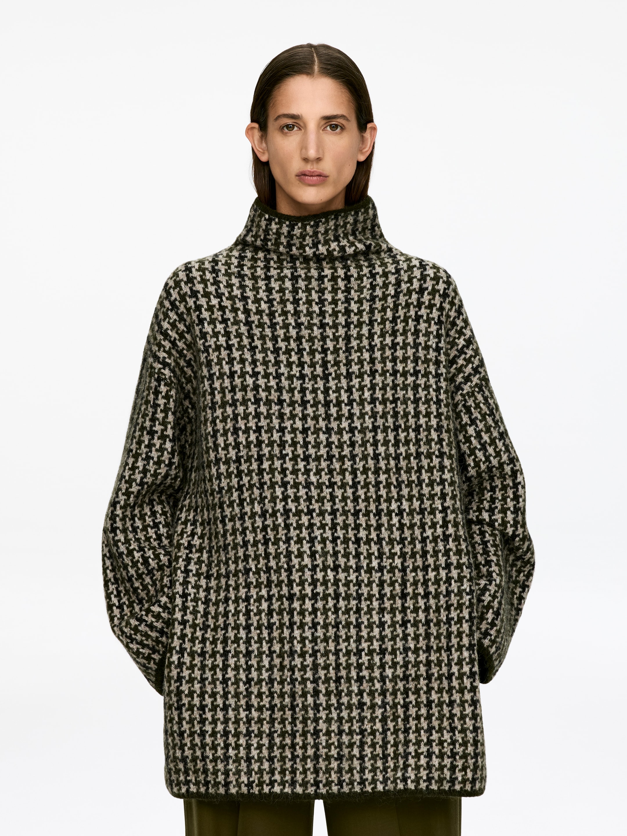 View larger image: A jacquard-knit jumper, displaying a green, black, and off-white houndstooth pattern, is being worn by the model. This long-sleeved style is featuring a mock neck and a relaxed fit, with the model's arms being kept within the garment.