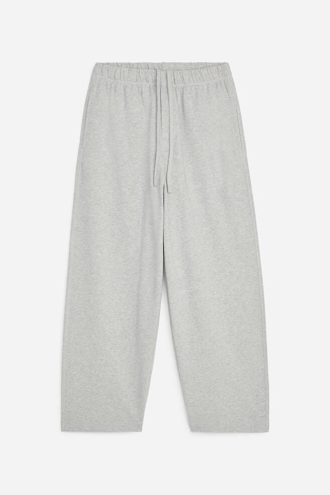 Ein Paar hellgraue, leger geschnittene Hosen ist frontal ausgerichtet und verfÃ¼gt Ã¼ber einen elastischen Bund mit verstellbarem Kordelzug sowie eine angedeutete ReiÃverschlussblende. Die Hose zeigt eine leicht zulaufende, weit geschnittene Silhouette mit Nahttaschen an den Seiten. - 1