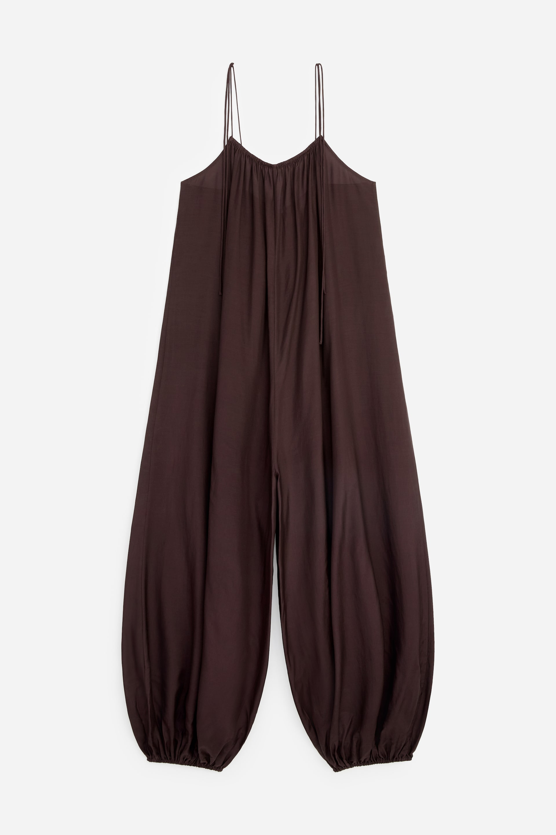 Größeres Bild ansehen: Der braune Jumpsuit präsentiert eine weite Ballonsilhouette mit einem gerafften Ausschnitt, schmalen, verstellbaren Spaghettiträgern und voluminösen Beinen, die an den Knöcheln gerafft sind.