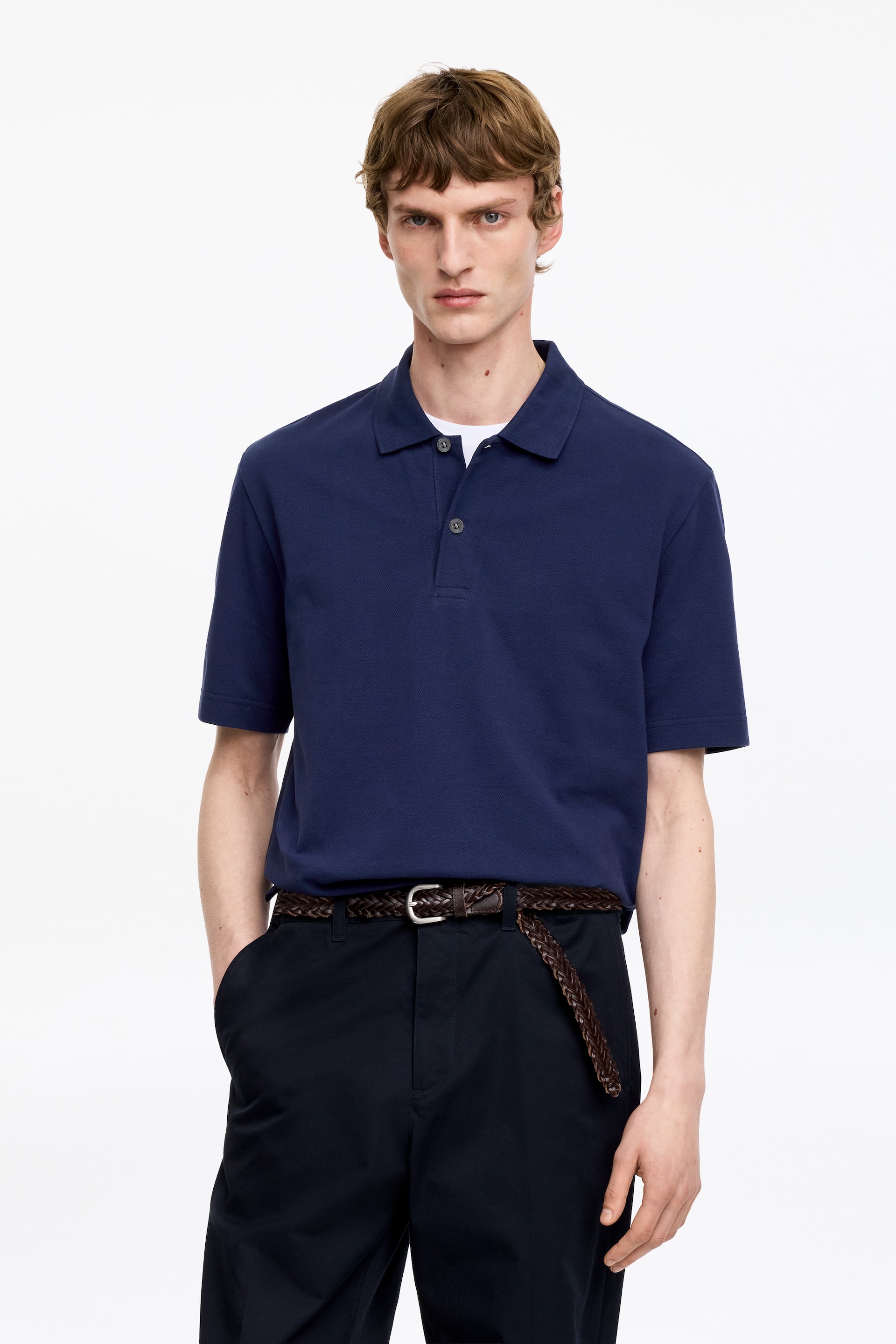 Ver imagen más grande: Una camiseta polo azul marino presenta un cuello extendido y una tapeta de dos botones, con mangas cortas. Se muestra de frente, superpuesta sobre una camiseta blanca.