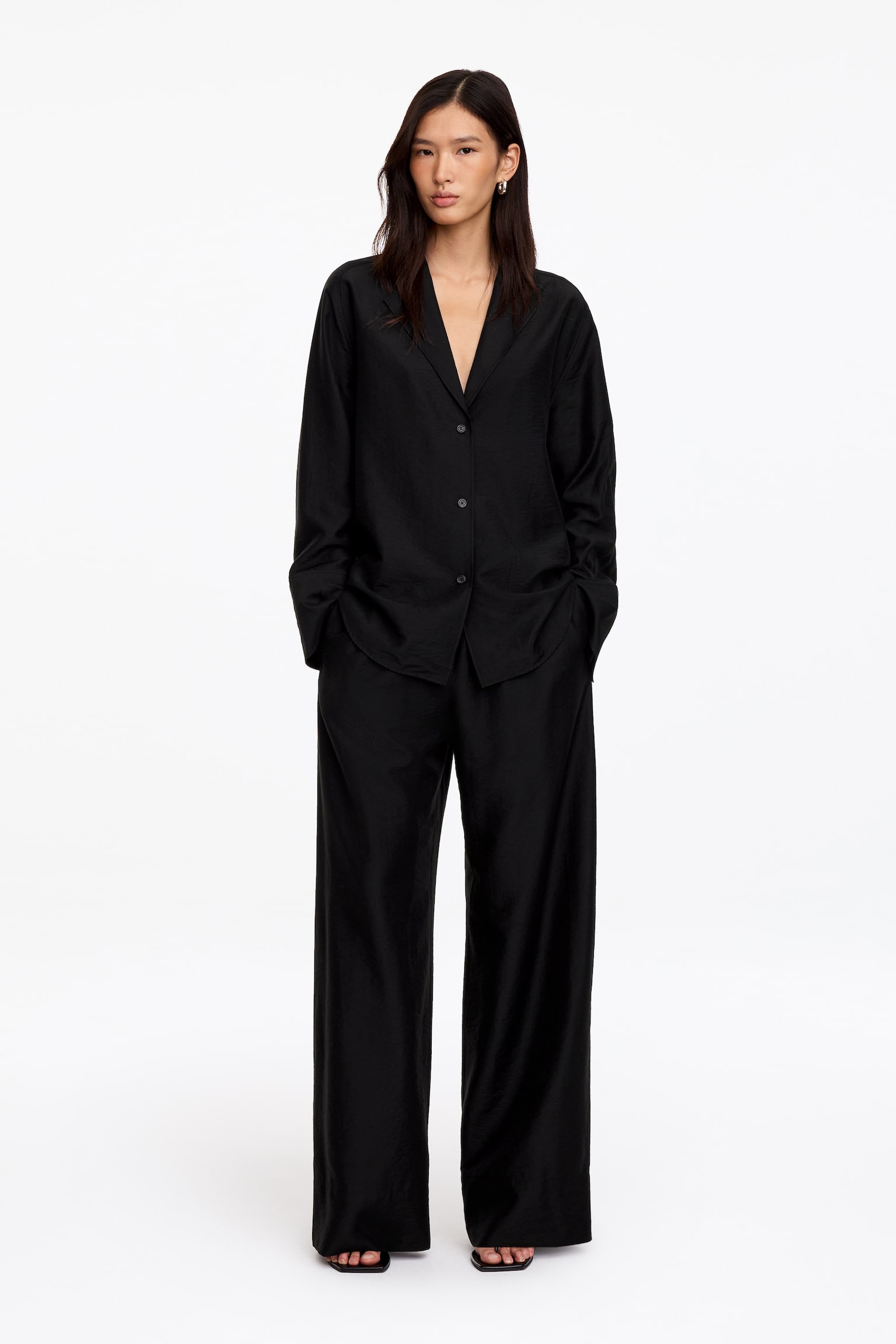 Eenvoudige zwarte broek, vervaardigd uit een lyocell-mix, gepresenteerd van voren. Ze zijn ontworpen met een elastische taille, zijnaadzakken en een enkele paspelzak aan de achterkant met knoopsluiting, en tonen een wijde pijp en een cropped silhouet. - 1