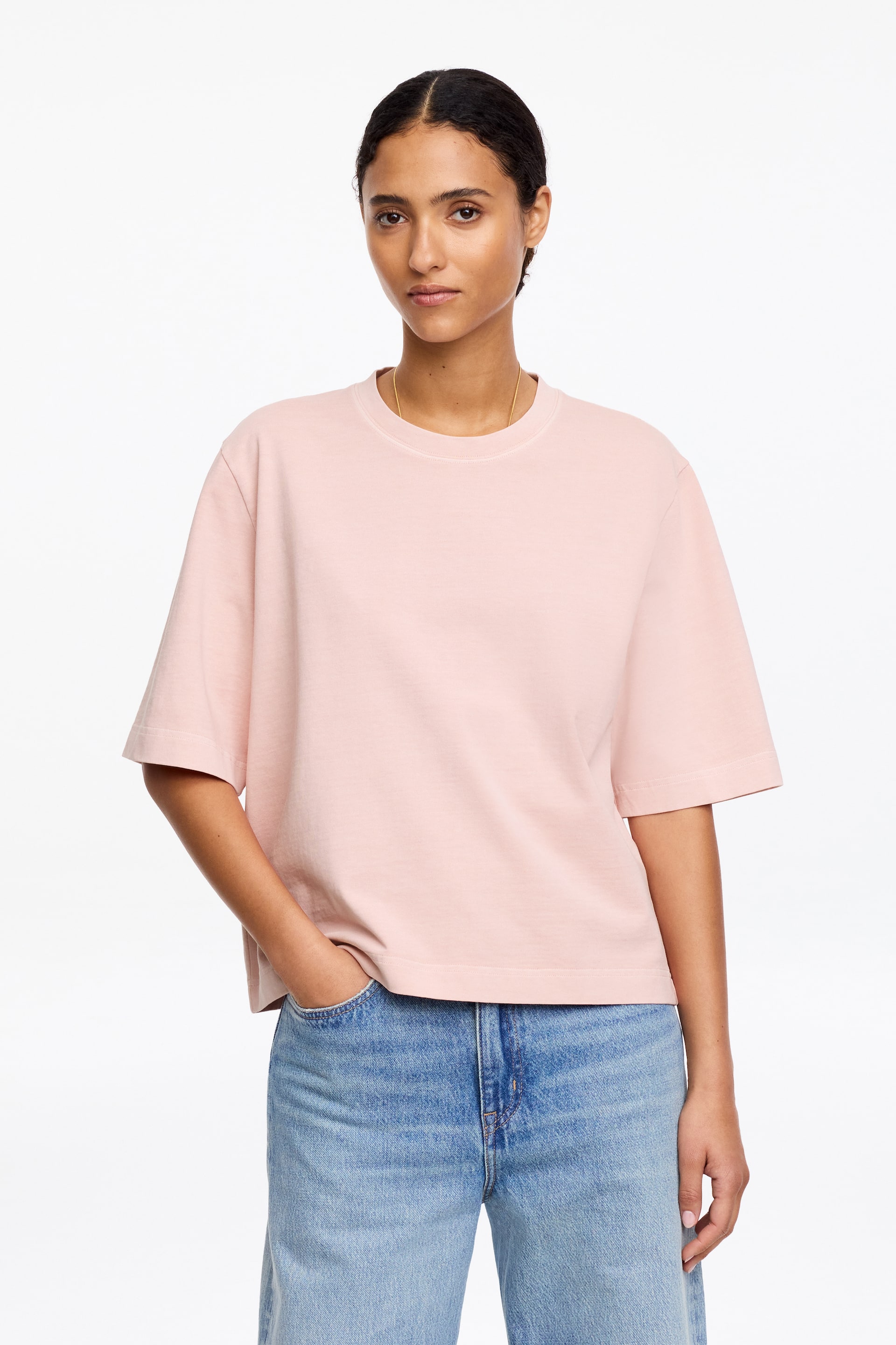 Προβολή μεγαλύτερης εικόνας: Ένα ροζ μπλουζάκι παρουσιάζεται με την μπροστινή όψη, διαθέτοντας στρογγυλή λαιμόκοψη, πλατιά κοντά μανίκια με καθαρές ραφές και χαλαρή εφαρμογή. Το ίσιο τελείωμα του πέφτει ακριβώς κάτω από τη μέση, ακουμπώντας πάνω από ανοιχτόχρωμο μπλε τζιν.
