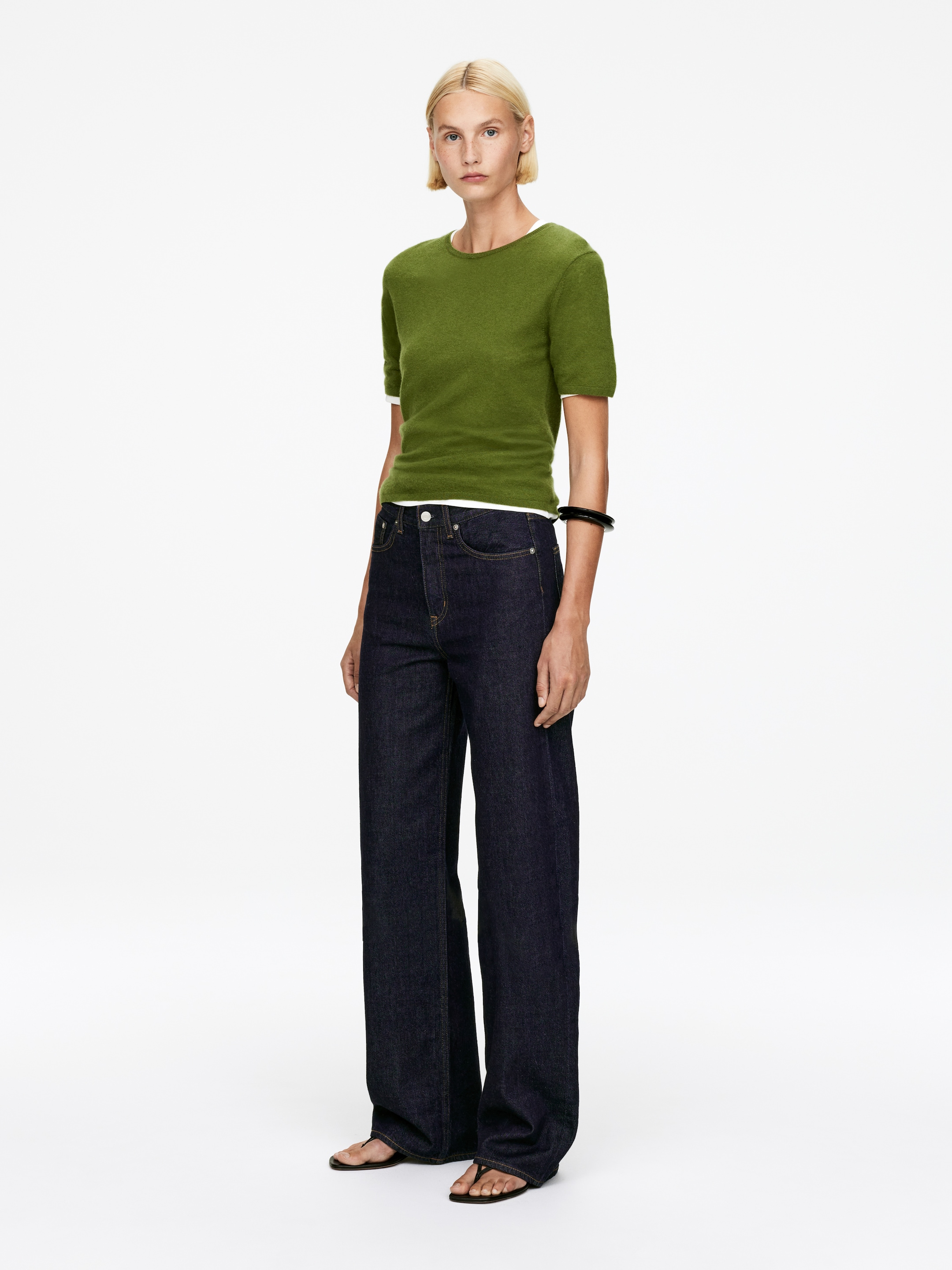 View larger image: A green short-sleeved top is being worn over a white garment, with the white fabric peeking out at the neckline and hem. Dark blue wide-leg jeans are being worn, featuring a relaxed fit and a subtle flare, with both products angled slightly to the right, revealing their front and side profiles.