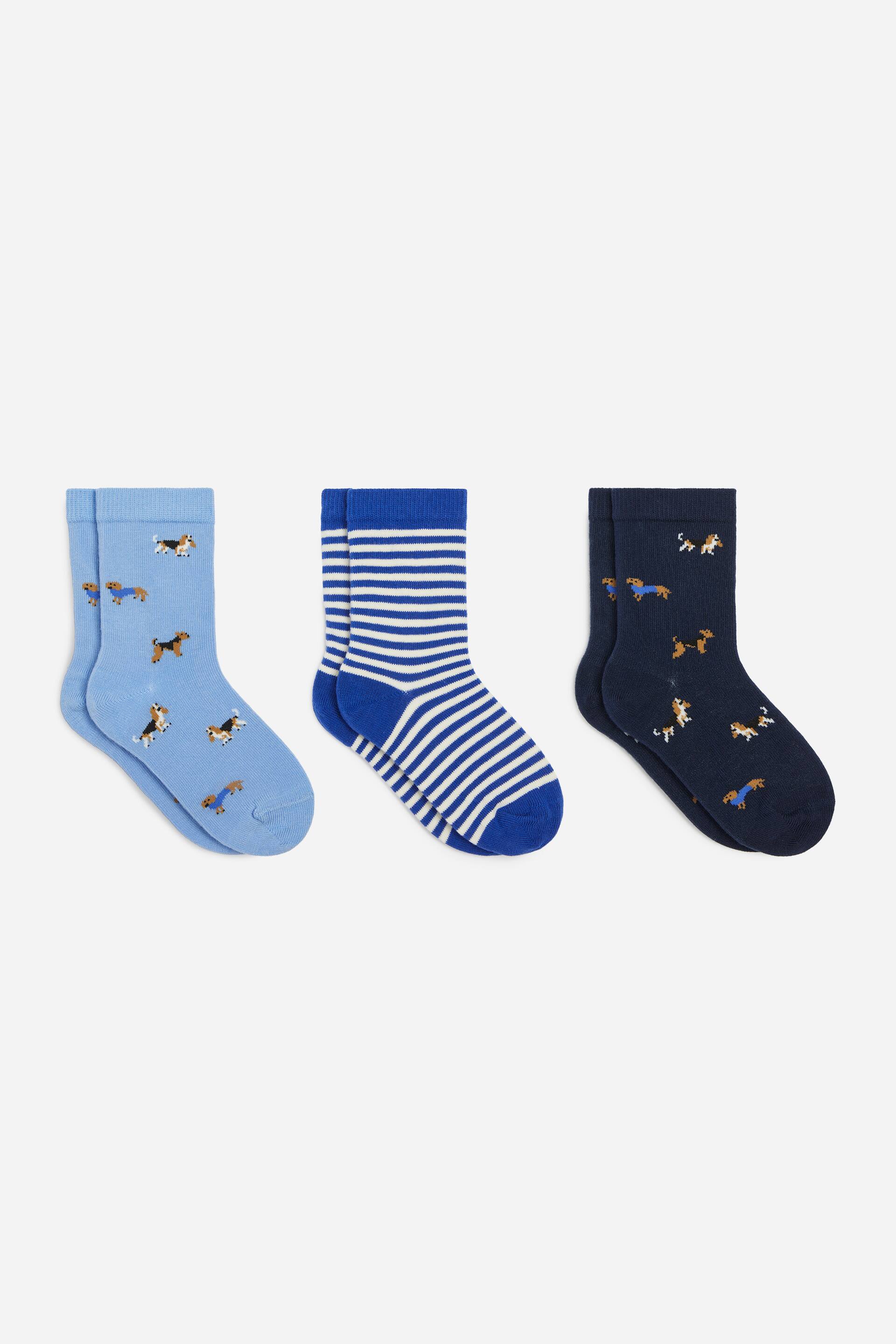 View larger image: Three pairs of socks are laid flat in a side-on view, each featuring ribbed cuffs. The set includes a light blue pair and a dark navy pair, both displaying an all-over pattern of small dogs, alongside a middle pair featuring horizontal royal blue and white stripes with solid blue cuffs, heels and toes.