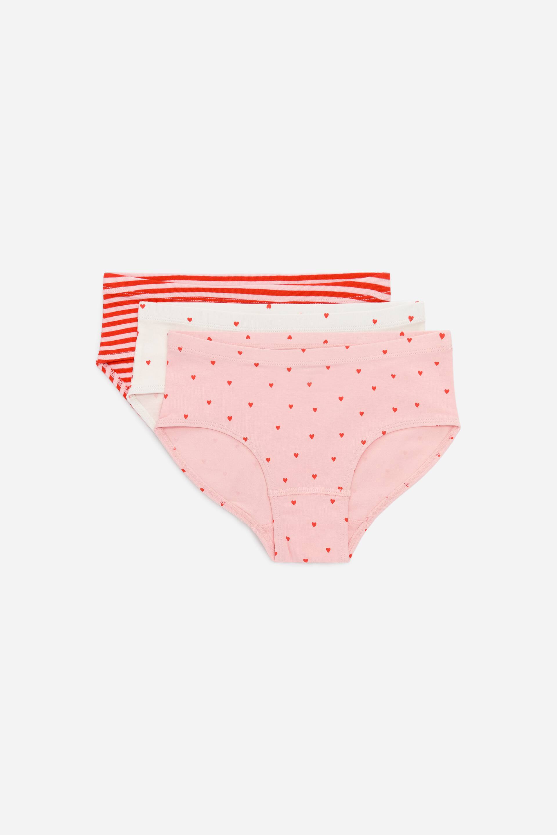 View larger image: Three pairs of briefs are neatly stacked, showcasing their fronts. The top pair features red and white horizontal stripes, the middle pair is a plain white, and the bottom pair is pink adorned with small red heart motifs.