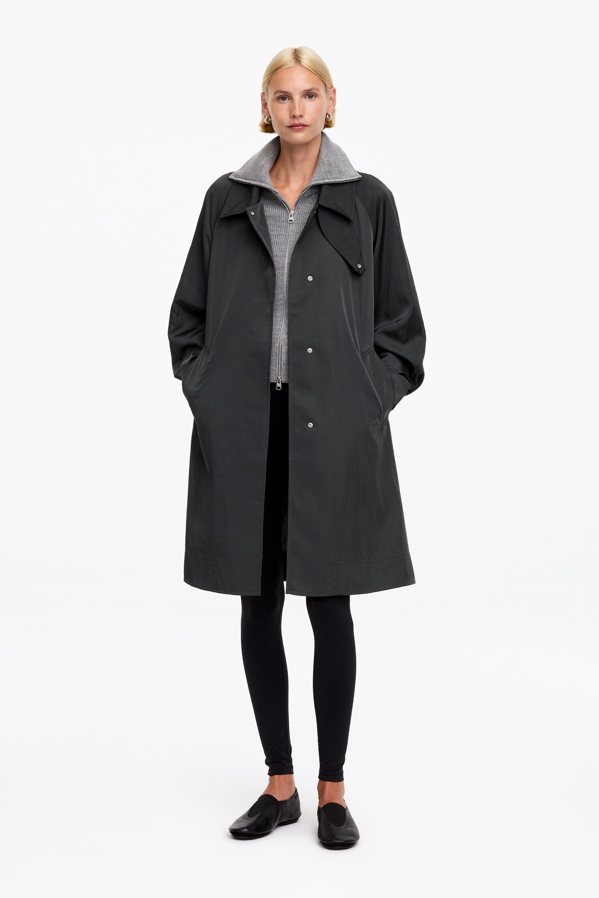 View larger image: A dark grey coat is being displayed from a front-facing angle, featuring a spread collar and a front snap button fastening. Two pockets are visible at the hips, and a grey ribbed cardigan is visible underneath, with its collar showing above the coat's collar.