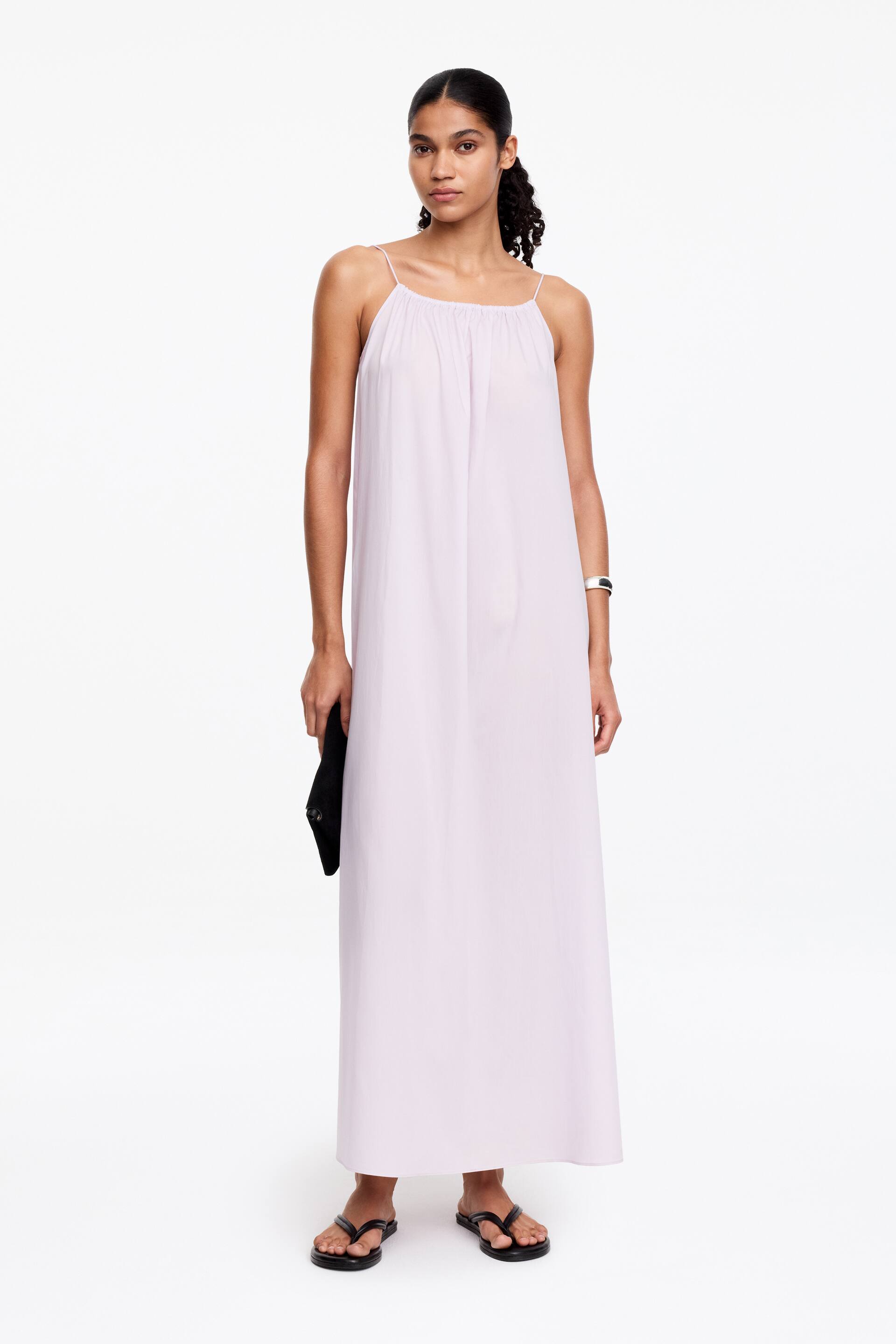 Agrandir l'image: La robe maxi mauve clair est conçue avec de fines bretelles spaghetti et un décolleté droit froncé. Elle est fluide dans une silhouette en A, s'étendant jusqu'au sol.