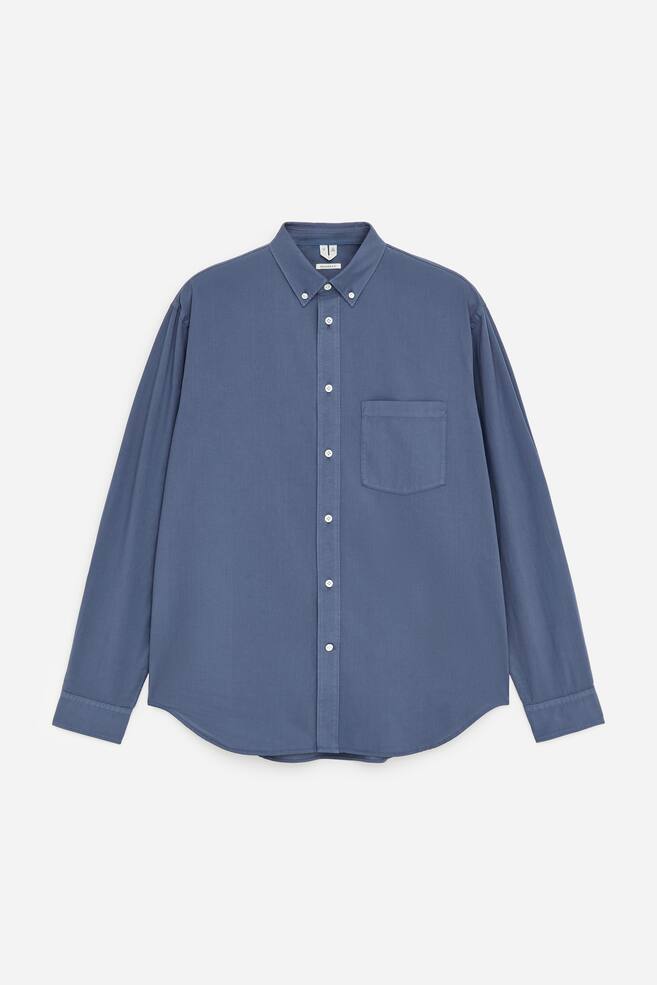 A blue long-sleeved shirt is presented FRONT, featuring a button-down collar, a full-button placket with white buttons, a single patch pocket on the left chest, long sleeves with buttoned cuffs, and a curved hem. - 1