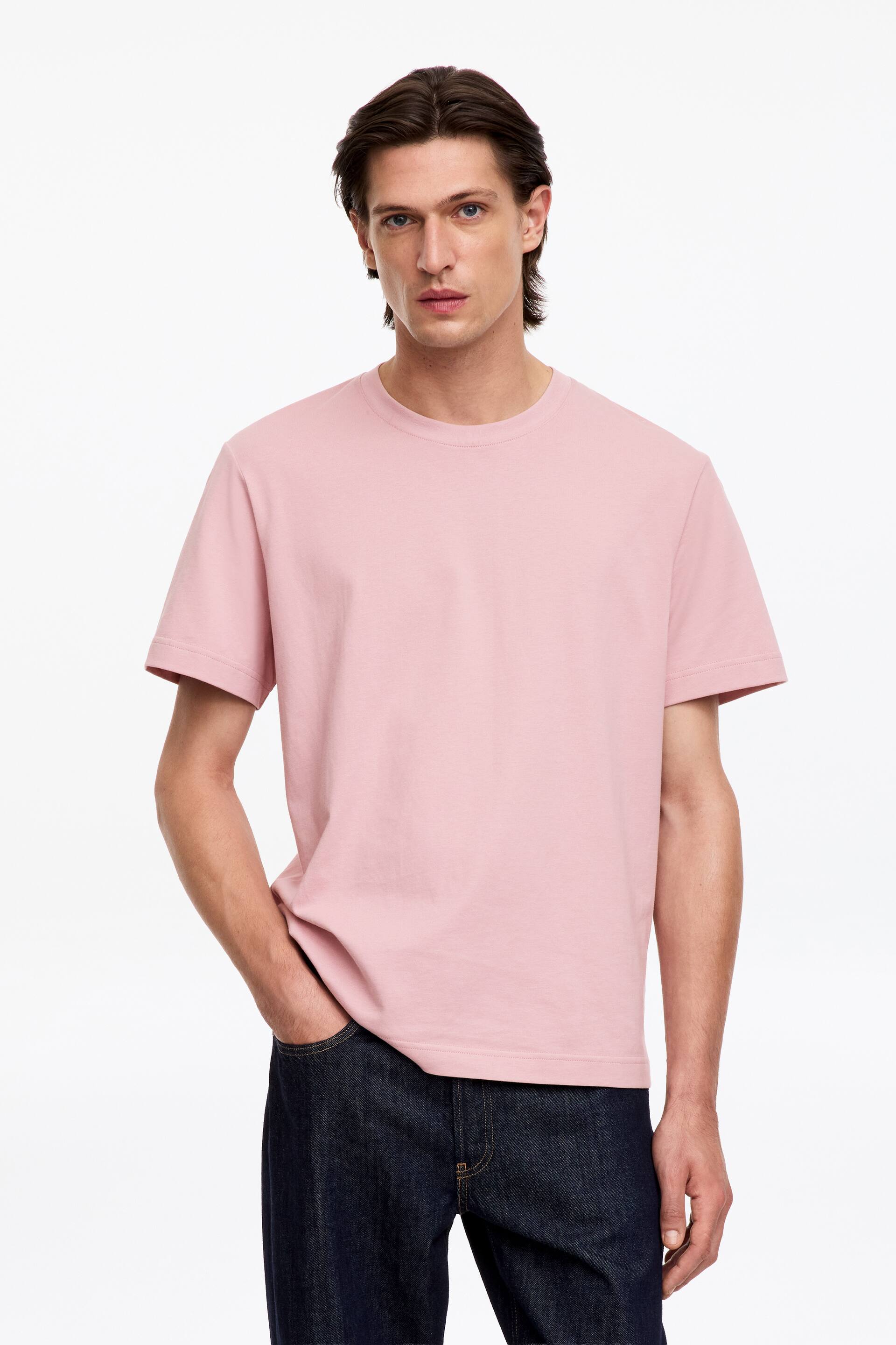 Agrandir l'image: Le mannequin porte un t-shirt rose à col rond, coupe décontractée et manches de longueur standard. Le mannequin est debout, une main glissée dans la poche d’un jean foncé.