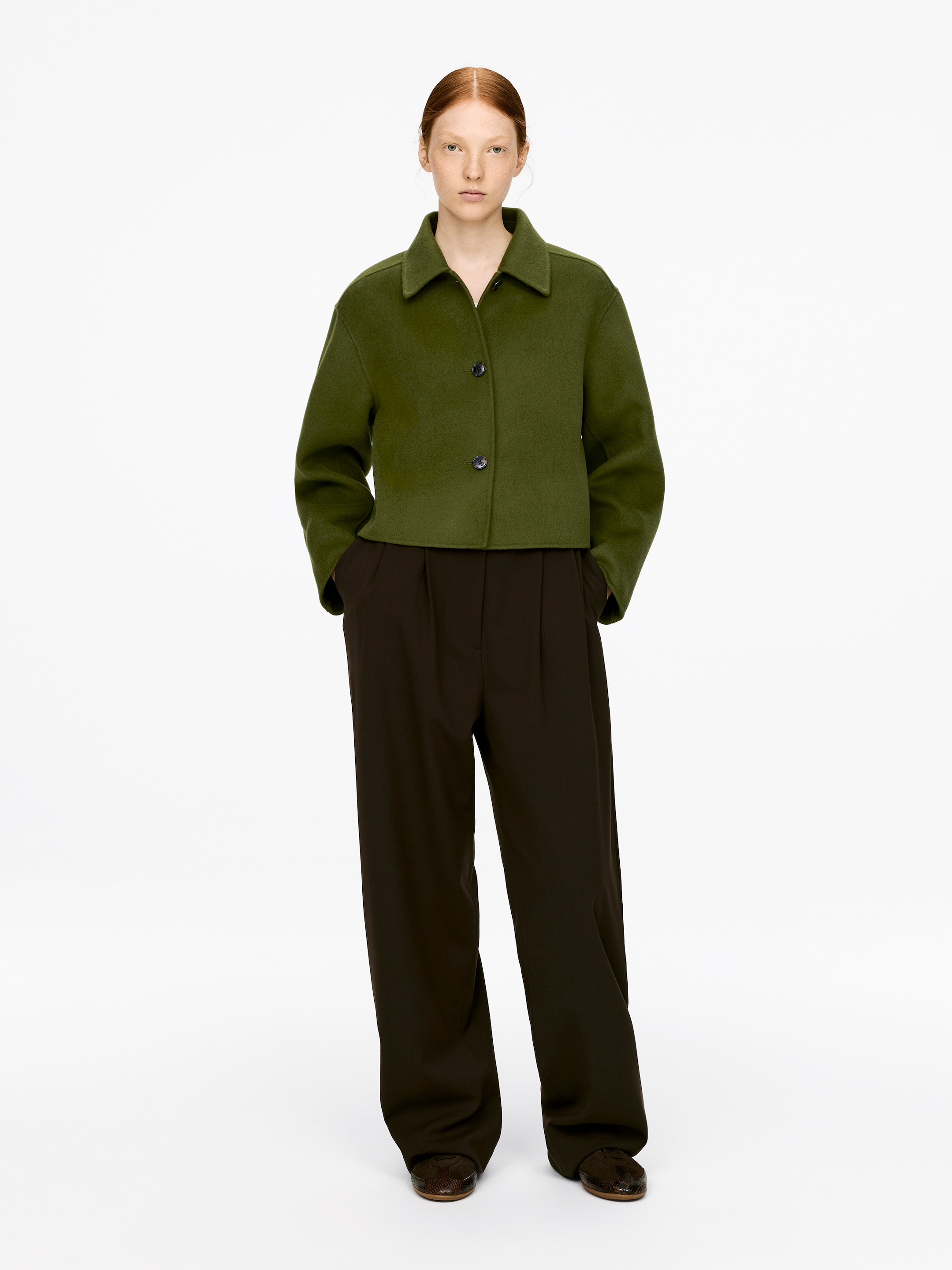 Ver imagen más grande: Una sobrecamisa verde oliva con cuello y cierre de botones frontales está siendo usada por la modelo. La sobrecamisa recortada de mezcla de lana presenta bolsillos donde las manos de la modelo están descansando.