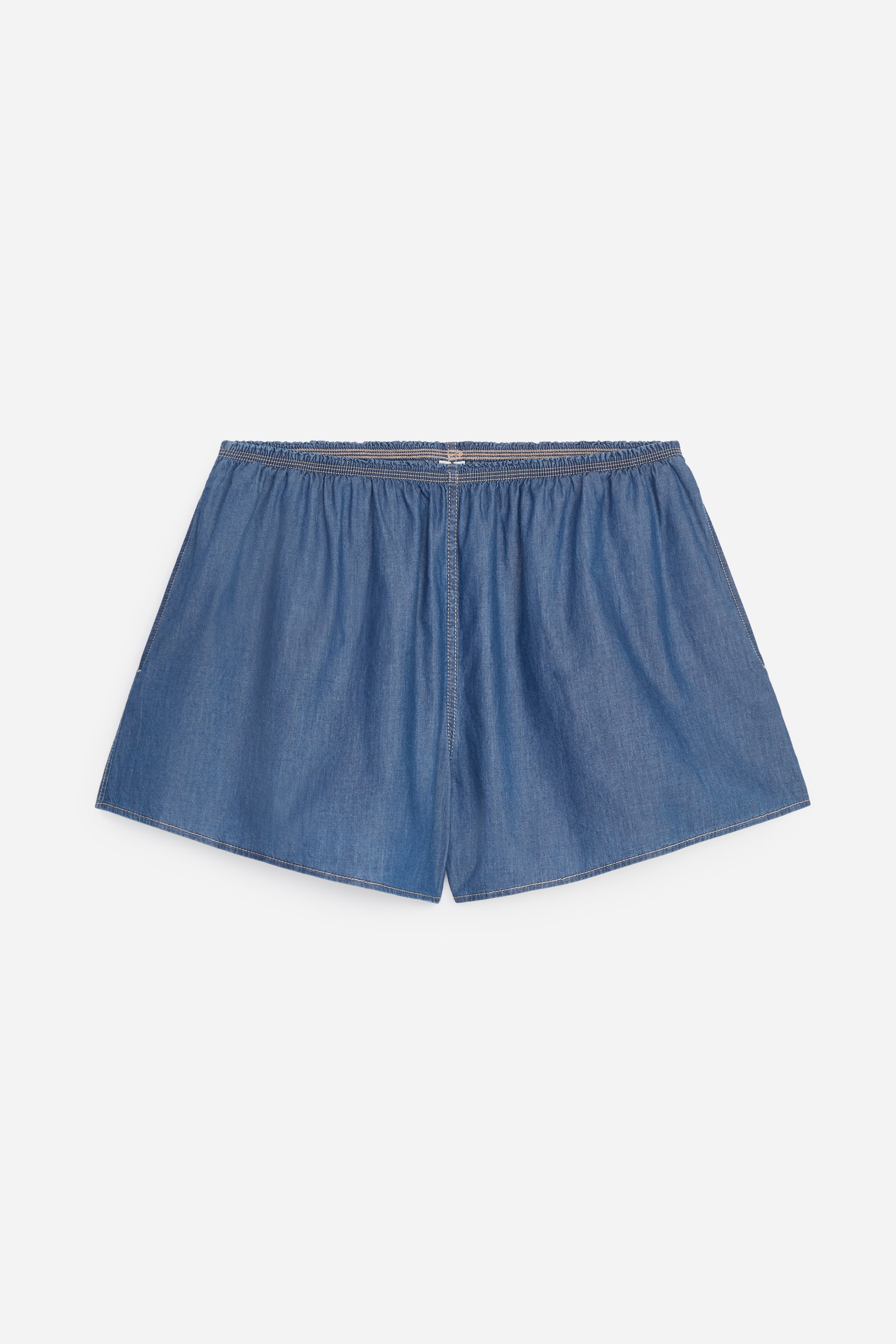 Vezi imaginea mai mare: Pantalonii scurți din denim albastru deschis, cu talie elastică, sunt așezați plat, prezentându-și fața. Aceștia au o talie elastică adunată, o croială clasică cu cusături verticale pe fiecare picior și un tiv dublu pliat.