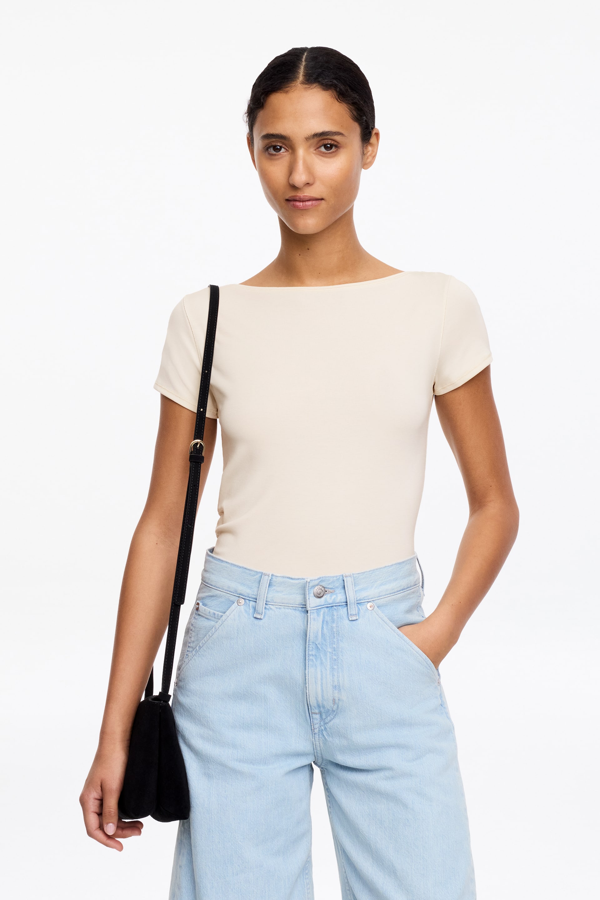 Visa större bild: Den ljusbeige toppen har en båtringning och korta ärmar. Den presenterar en slät, figurnära siluett, tydligt instoppad i ett midjeband.