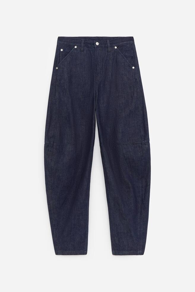 The front of the dark blue denim jeans showcases a mid-rise waist, a relaxed fit and tapered legs. It features a zip fly closure, angled front pockets with visible rivets and horizontal seam detailing on the upper legs. - 1