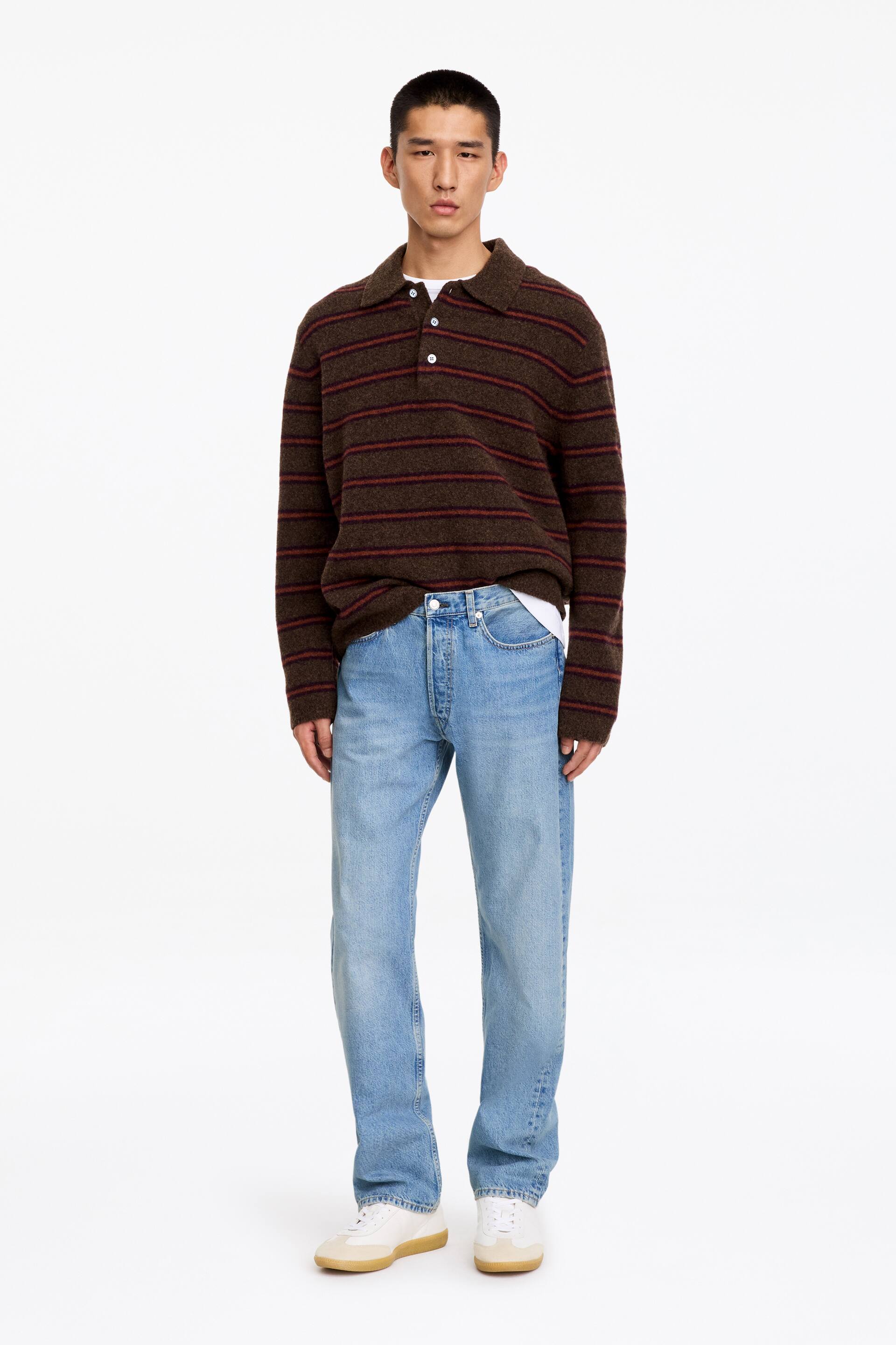 Vis større bilde: Lyseblå, rette denimjeans med middels høy midje og regular fit bæres av modellen. Jeansene er stylet med en brun stripete poloskjorte delvis stukket ned i livet og hvite sneakers.