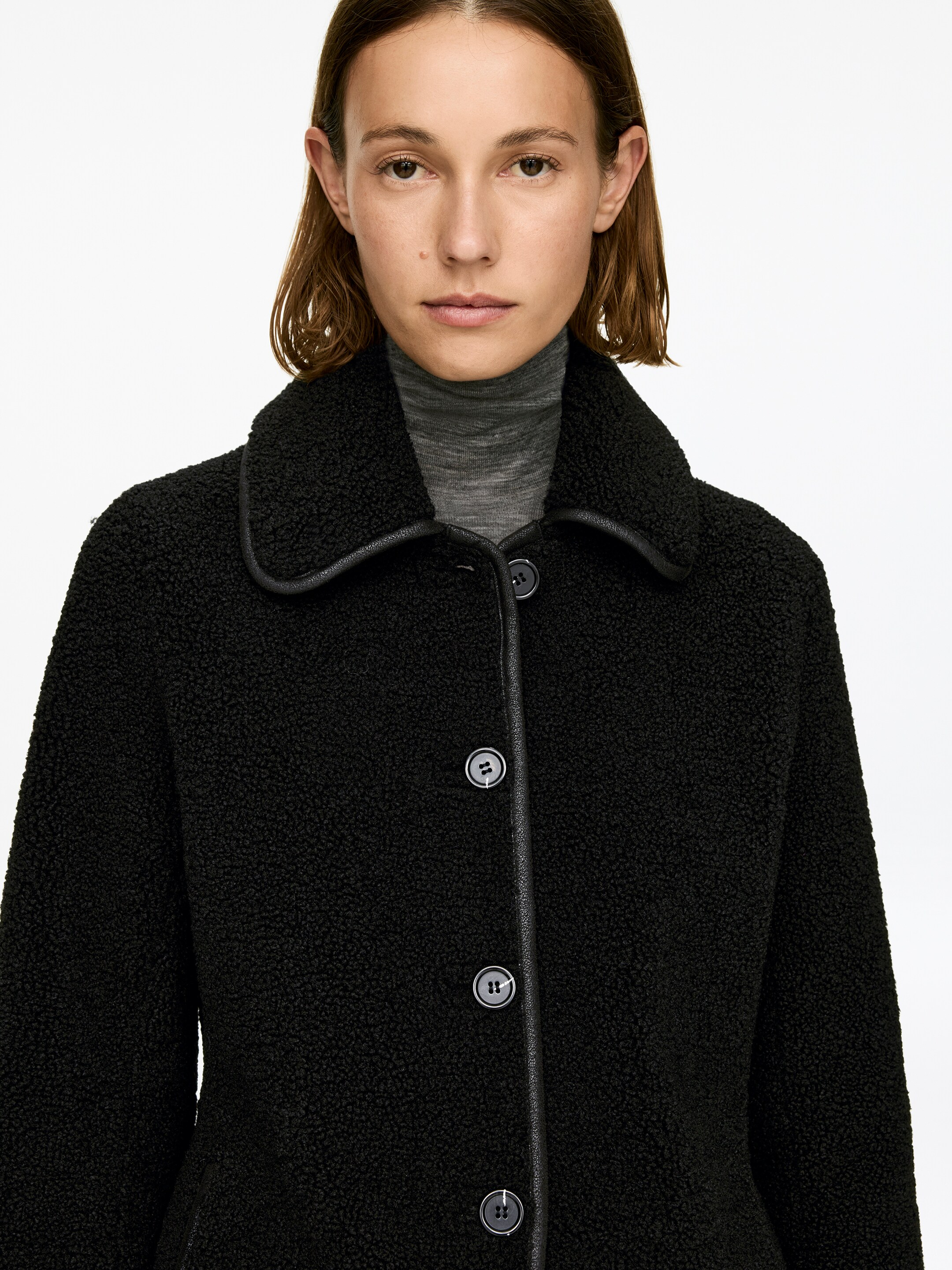 View larger image: A black single-breasted pile jacket is being worn by the model, featuring a classic collar and front button closure accented with black trim. A grey turtleneck sweater is worn underneath.