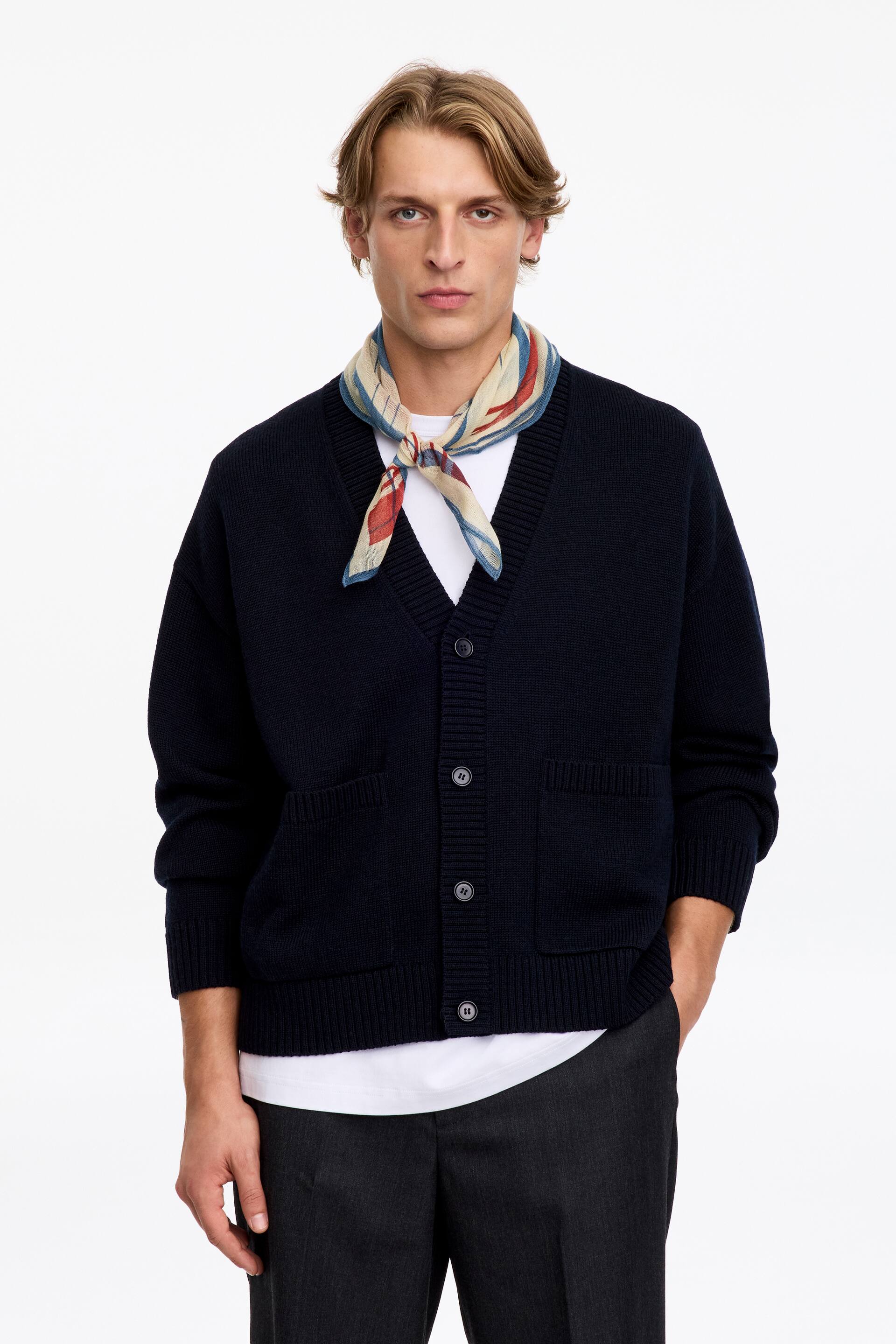 Agrandir l'image: Une écharpe en laine à motif à carreaux dans des tons jaune, rouille-orange et bleu est portée nouée autour du cou du mannequin. L’écharpe est stylisée sur un t-shirt blanc et superposée sous un cardigan bleu marine boutonné.