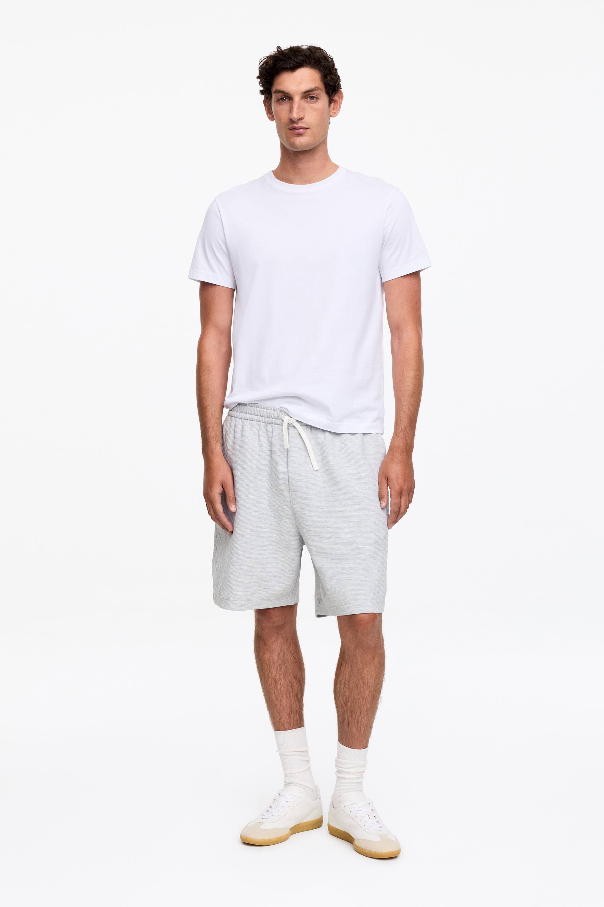 Agrandir l'image: Un t-shirt blanc à manches courtes et un short gris chiné avec cordon de serrage sont présentés de face. Le t-shirt est doté d'un col rond, et le short a une coupe décontractée, se terminant au-dessus du genou.