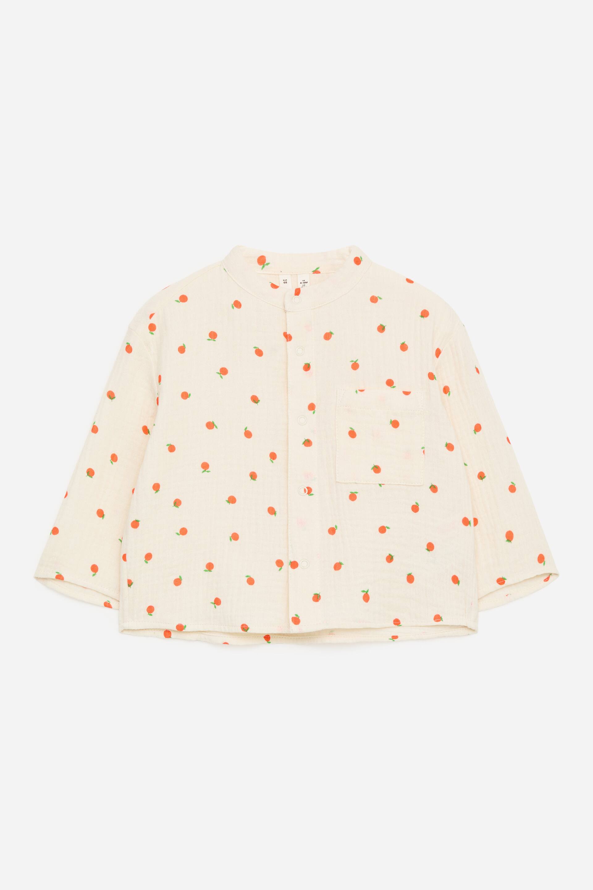 Größeres Bild anzeigen: Das kragenlose Hemd wird von vorne präsentiert, gefertigt aus cremefarbenem Baumwoll-Musselin und mit einem sich wiederholenden Muster kleiner orangefarbener Früchte. Es ist mit einer durchgehenden Knopfleiste, einer einzelnen aufgesetzten Tasche auf der linken Brust und langen, locker geschnittenen Ärmeln gestaltet, was ihm insgesamt eine entspannte Passform verleiht.