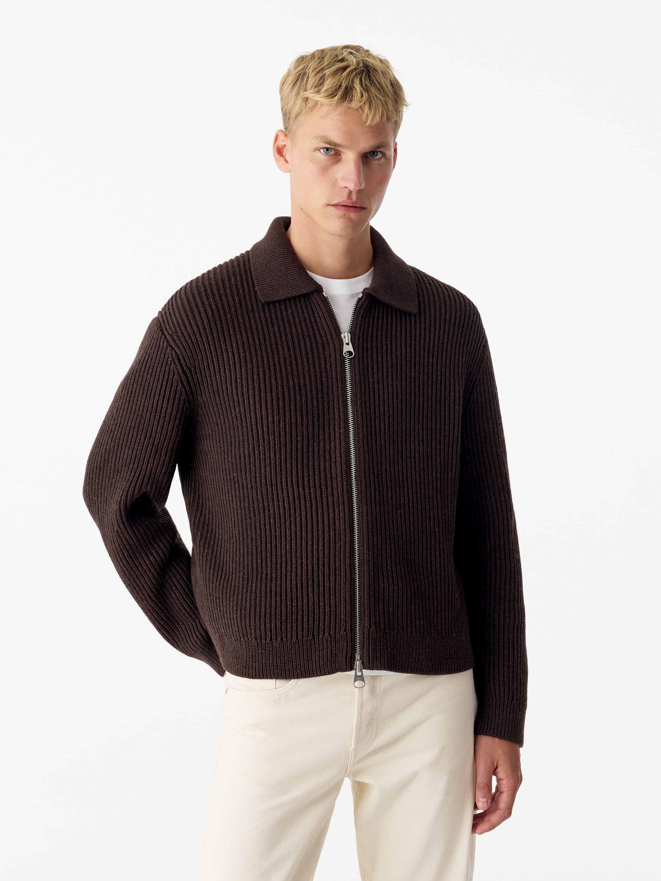 A dark brown ribbed-knit zip-up cardigan is shown from the front, featuring a spread collar and a full-length silver zip fastening. The garment has long sleeves, ribbed cuffs and a matching ribbed hem.