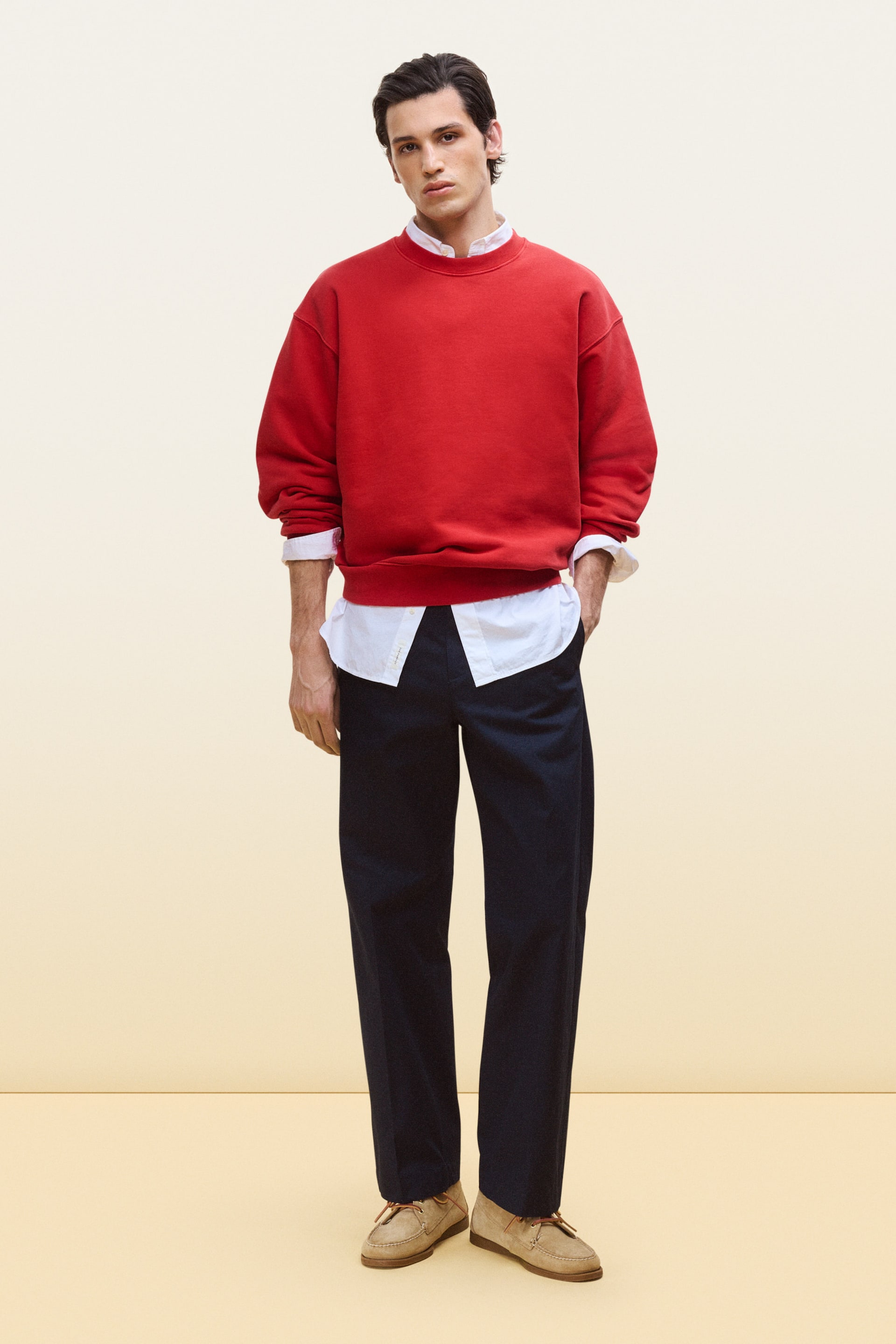 Visa större bild: En röd crewneck-tröja visas framifrån, med en avslappnad passform och ribbad krage, ribbade muddar och ribbad fåll. Den bärs i lager över en vit skjorta med krage, där skjortans krage och manschetter syns tydligt underifrån.