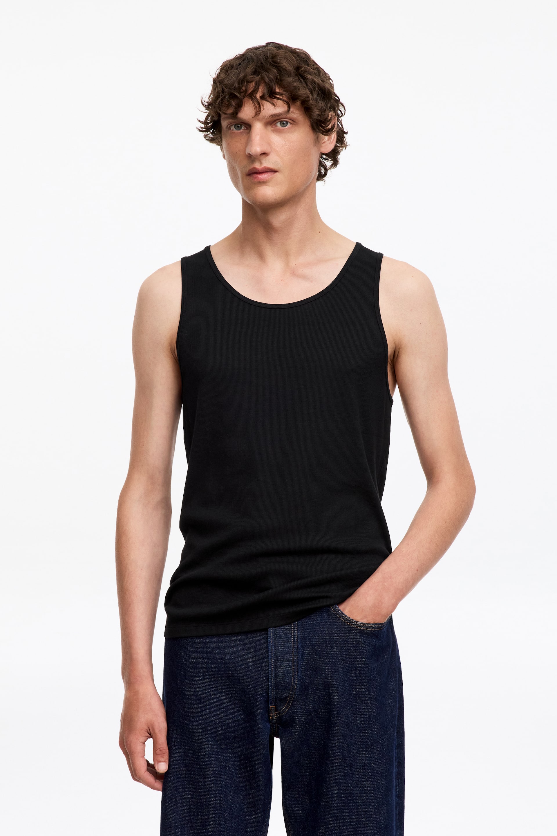 Grotere afbeelding bekijken: Een zwarte geribbelde jersey tanktop wordt gedragen door het model. De tanktop heeft een ronde hals en is ingestopt in donker gewassen jeans.