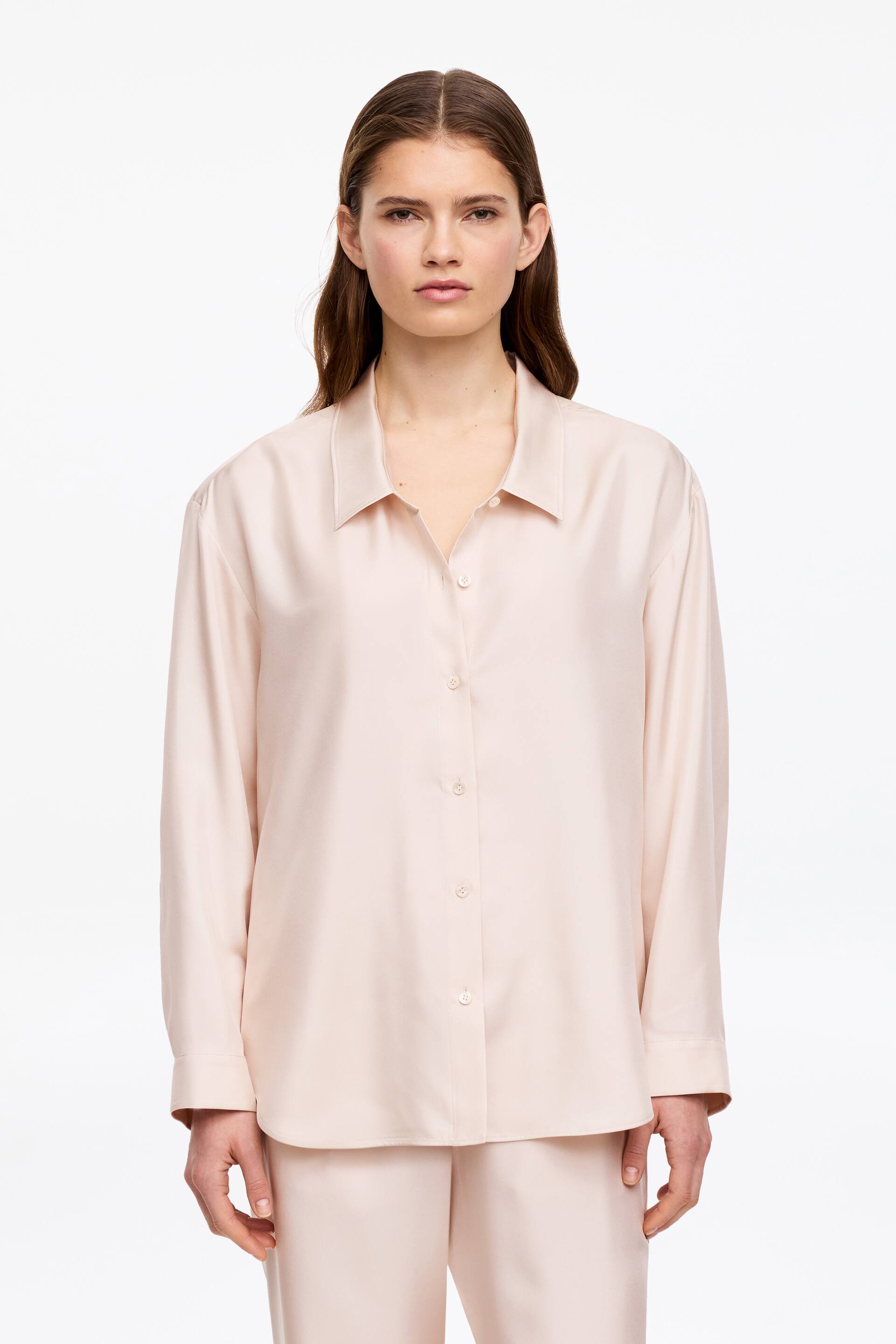 Преглед на по-голямо изображение: "Чиста копринена риза с ниска яка, закопчаване с копчета и извито подгъване, носена от модела. Моделът също носи съответстващи панталони."