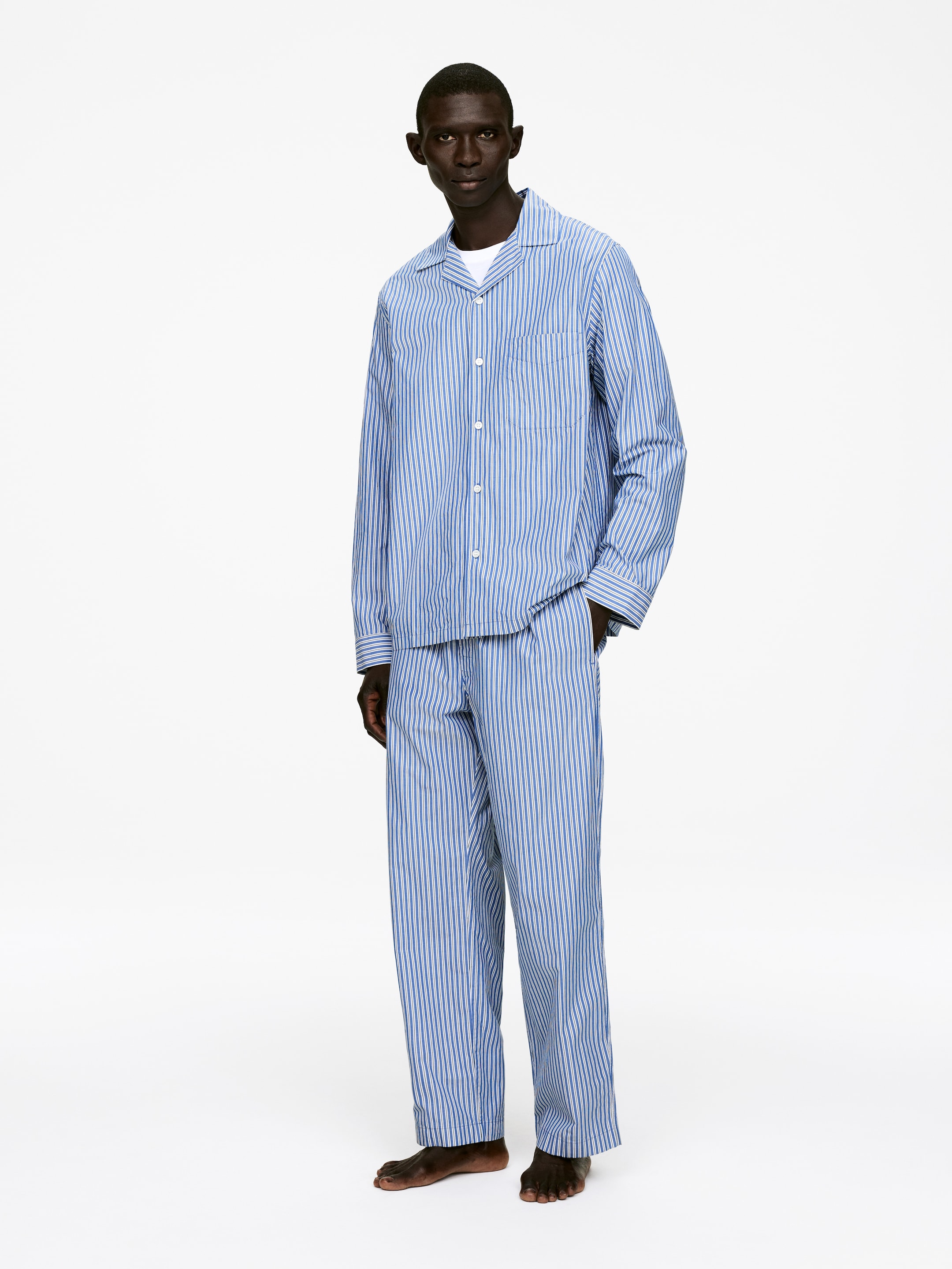 Agrandir l'image: Un ensemble de pyjama à rayures verticales bleu clair et bleu foncé est présenté en vue complète. Le haut boutonné à manches longues présente un col à revers et une poche poitrine unique, et est porté sur un t-shirt blanc avec un pantalon droit assorti.