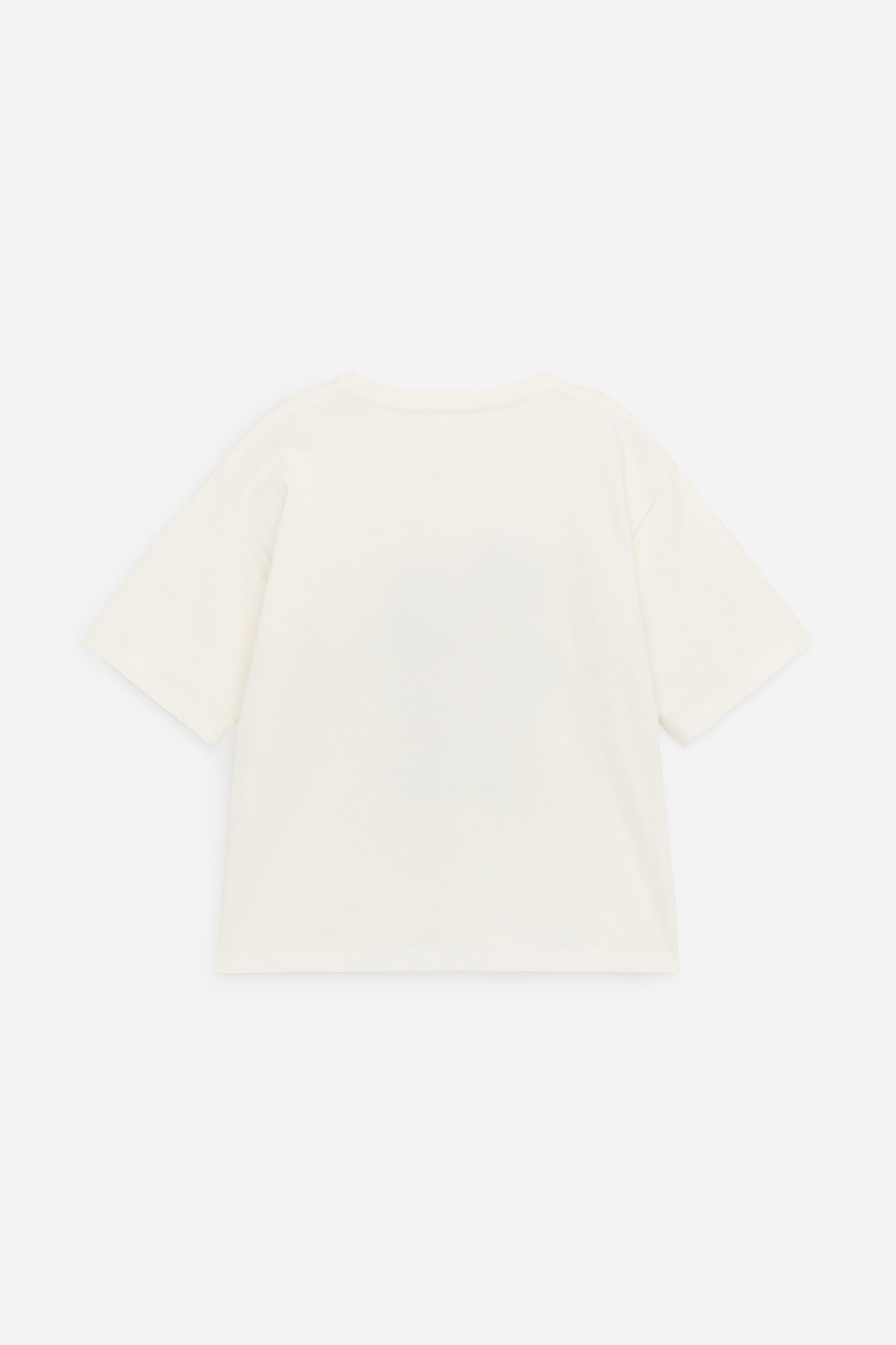 Ver imagem maior: Uma t-shirt de cor creme claro é exibida de costas. Apresenta uma gola redonda, mangas curtas e ombros ligeiramente caídos, proporcionando um ajuste oversized.
