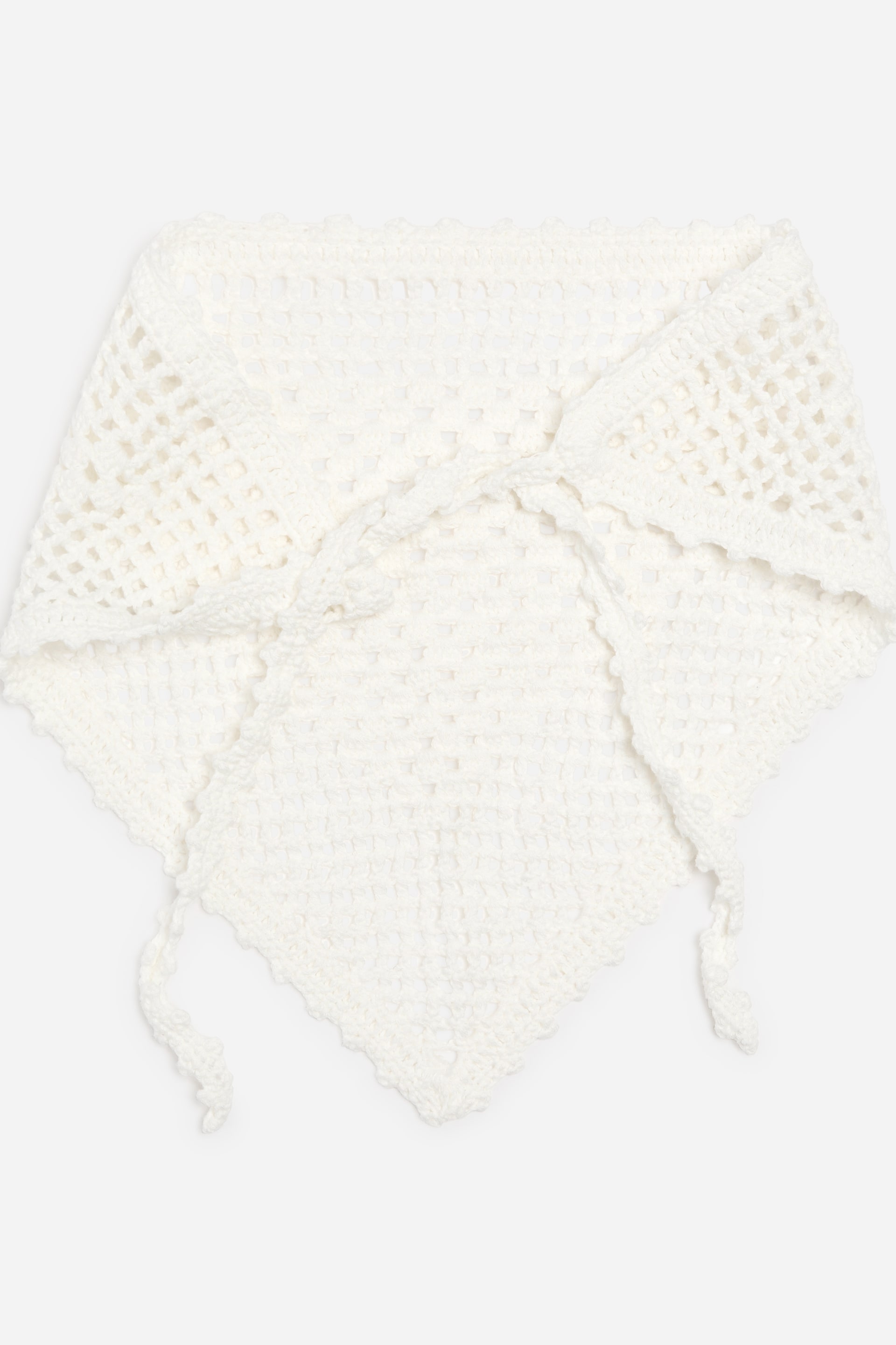 Grotere afbeelding bekijken: Een witte gehaakte driehoekige bandana toont een open-mesh patroon op de grotere buitenste delen en een dichtere haaksteek op het centrale paneel. De randen zijn afgewerkt met een geschulpte rand, en twee gehaakte linten worden bovenaan geknoopt.
